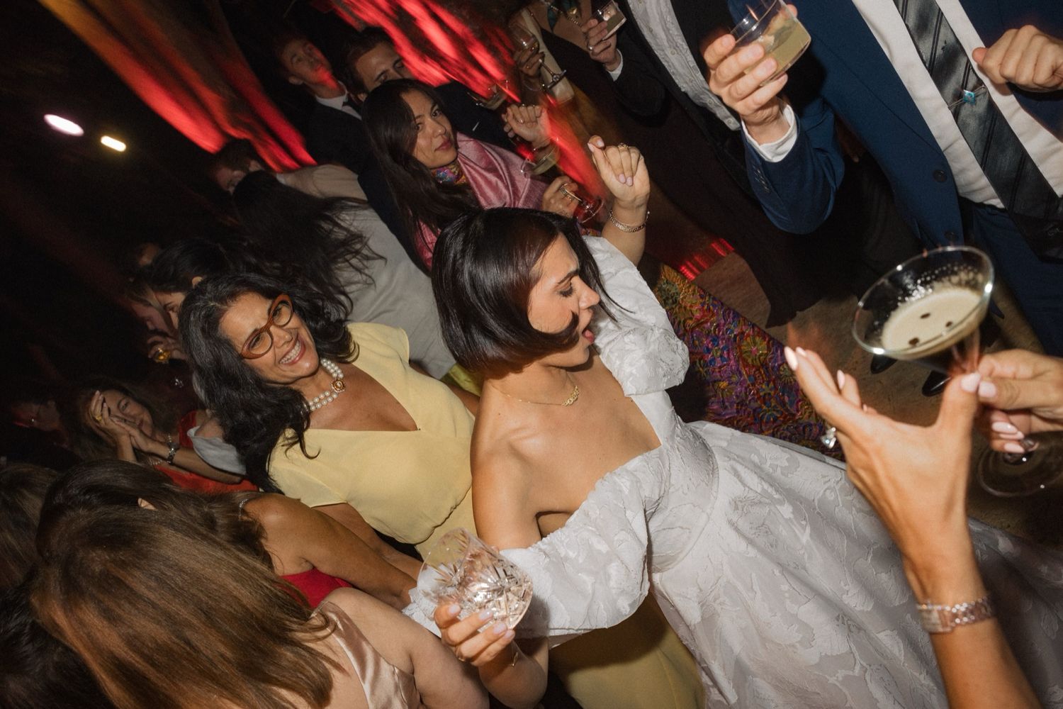 People dancing and enjoying themselves at a nightclub with red lighting and dark ambiance.