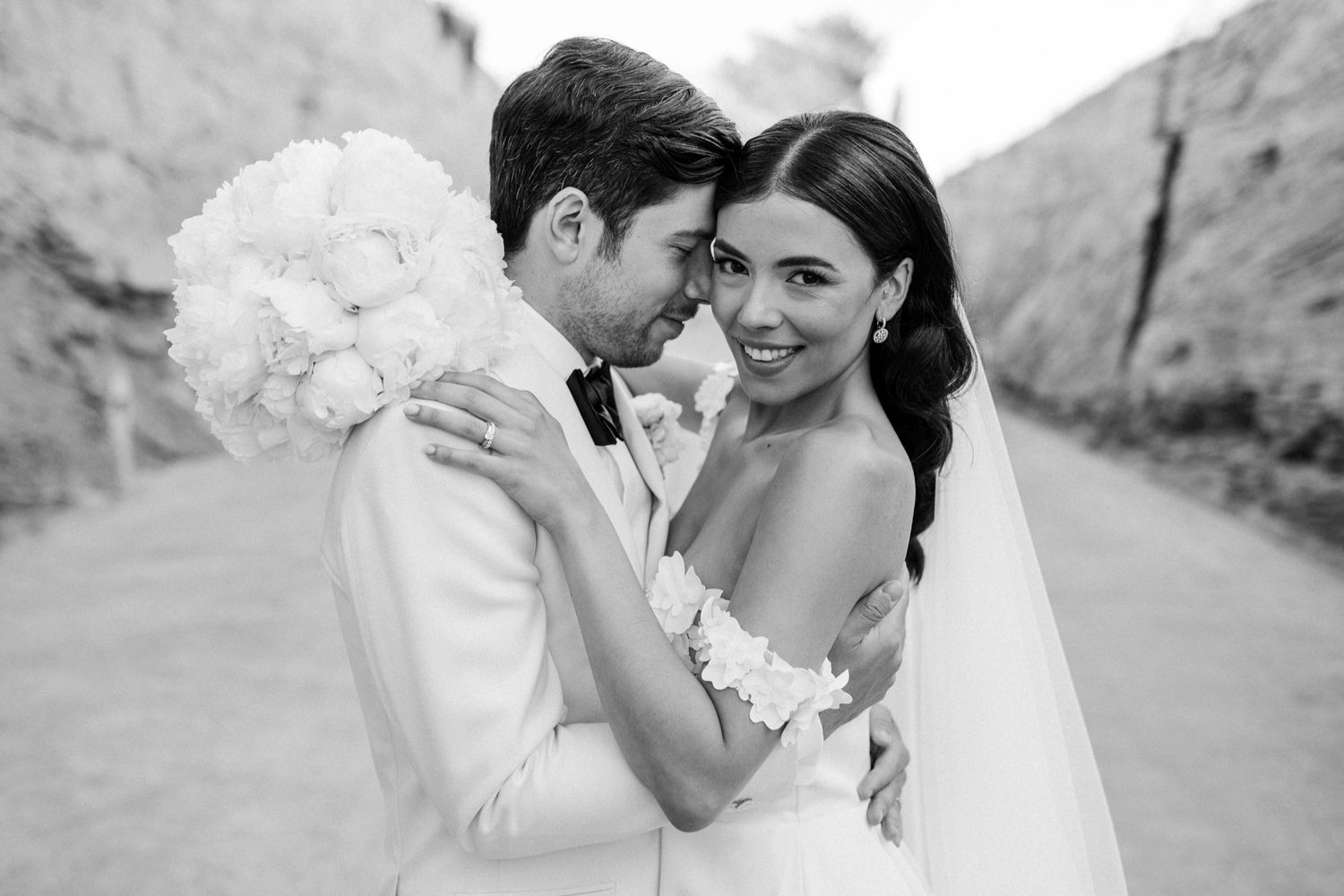 Black and white wedding photo of bride and groom touching foreheads, bride holding white bouquet.