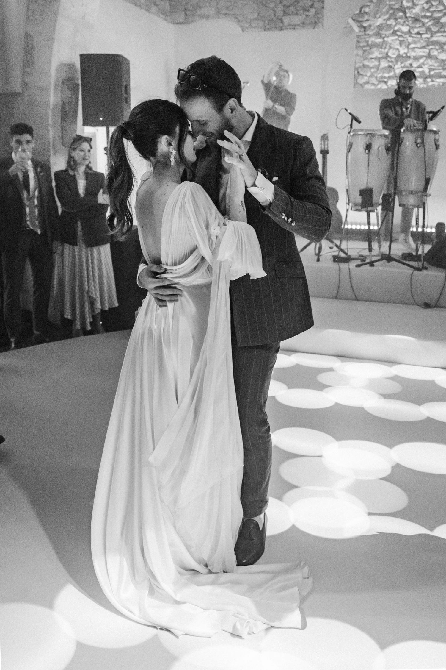 A couple performs their first dance at a wedding reception, with the bride in a flowing white gown under dramatic lighting.