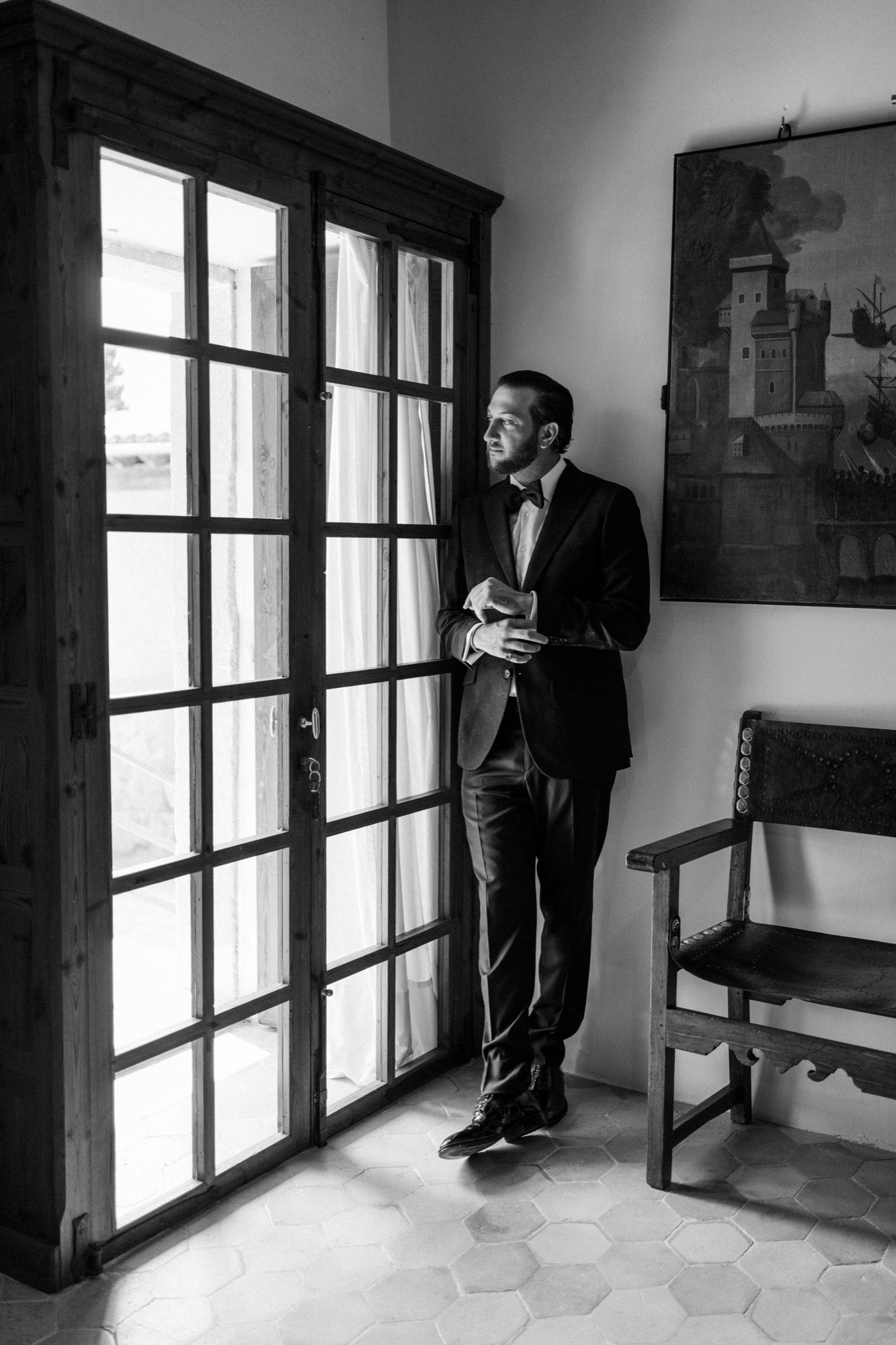 Black and white sequence of a suited figure standing by large windows in an elegant interior space.