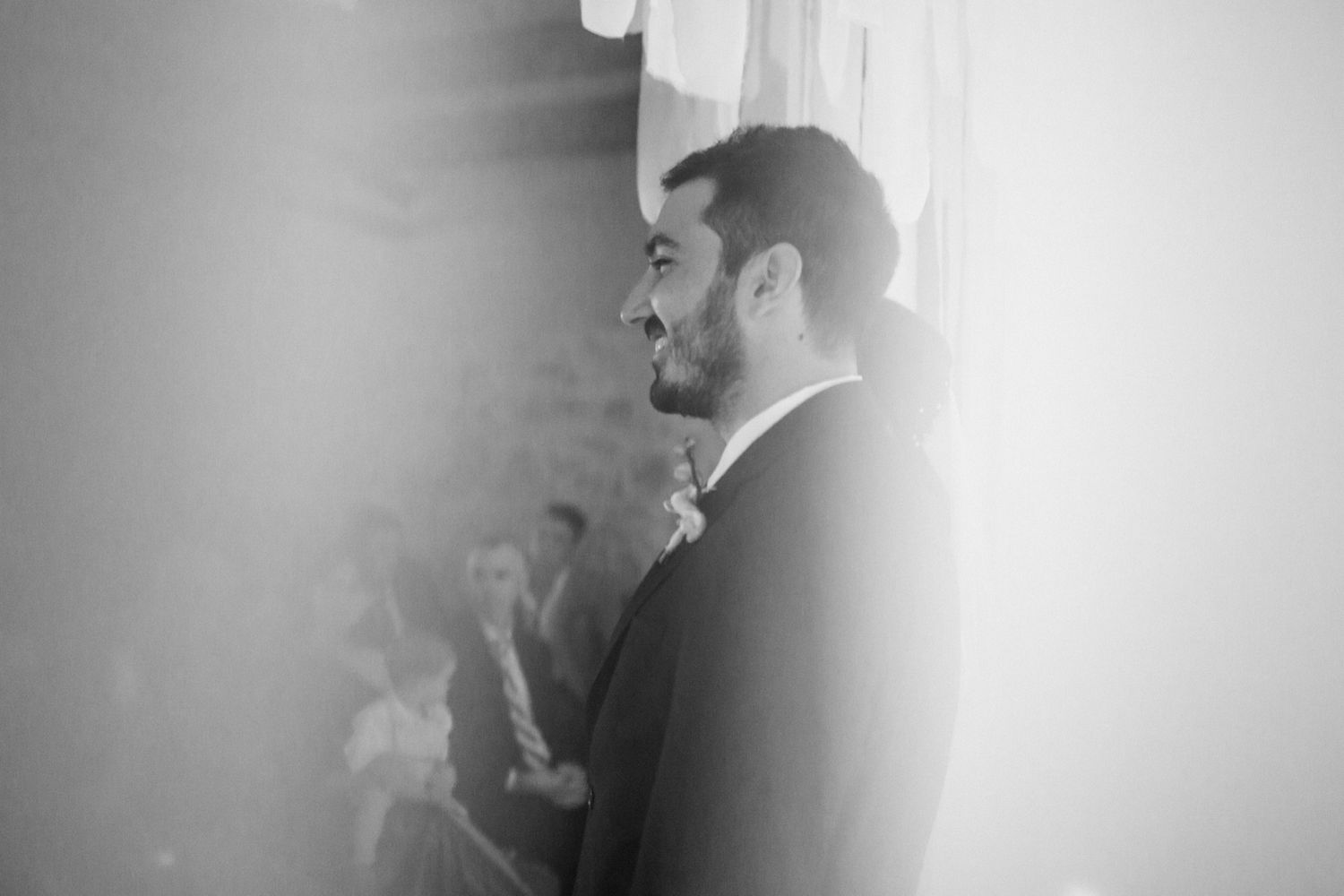 Black and white profile view of a groom in a formal suit during a wedding ceremony.
