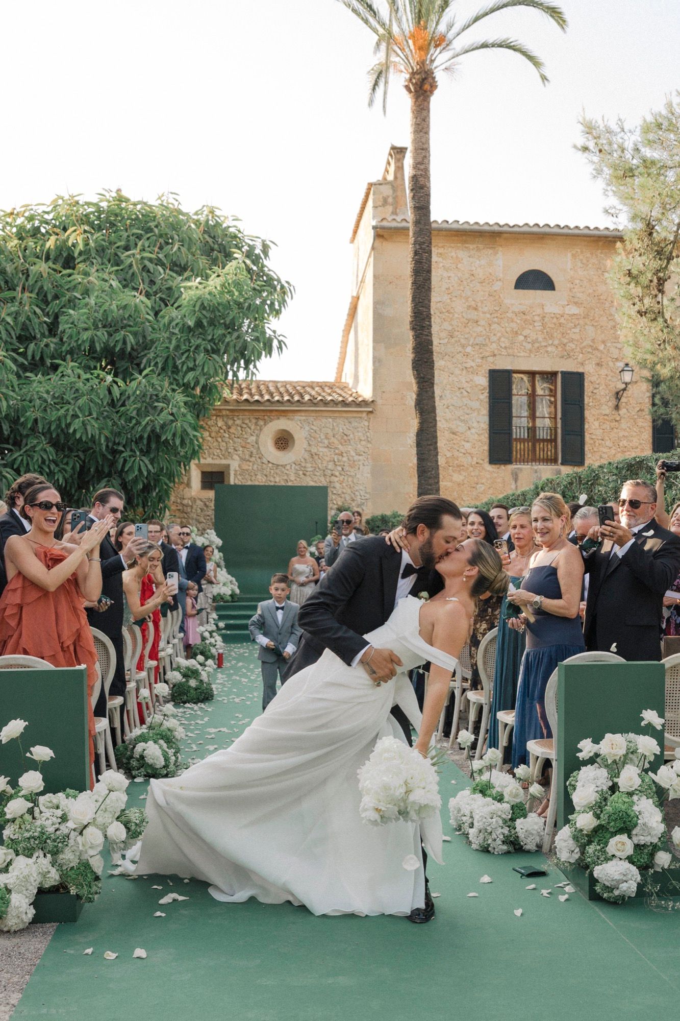 Wedding celebration on green floor with white floral arrangements and palm trees.