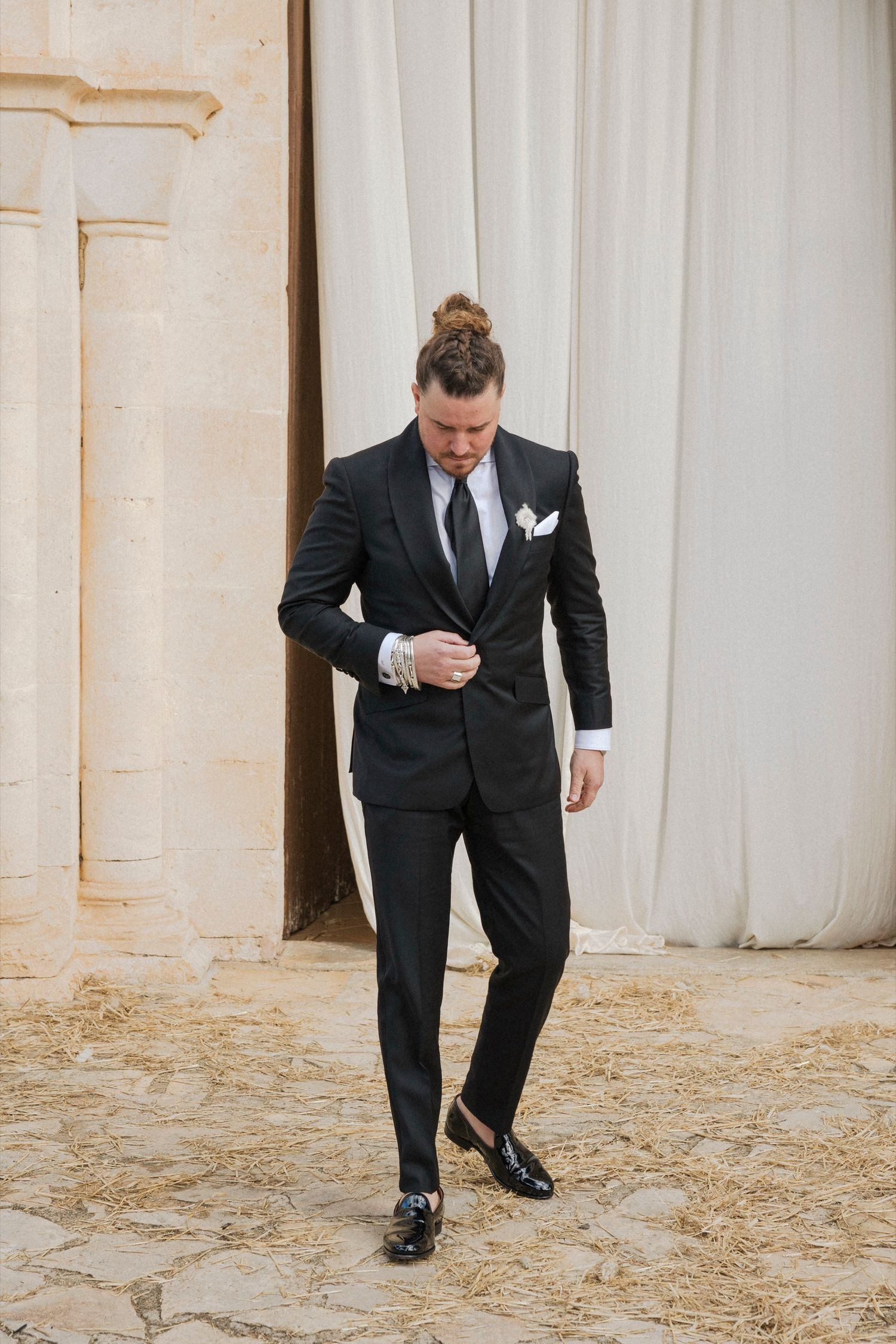 Person in a black suit bending down to adjust their shoe during a formal event.