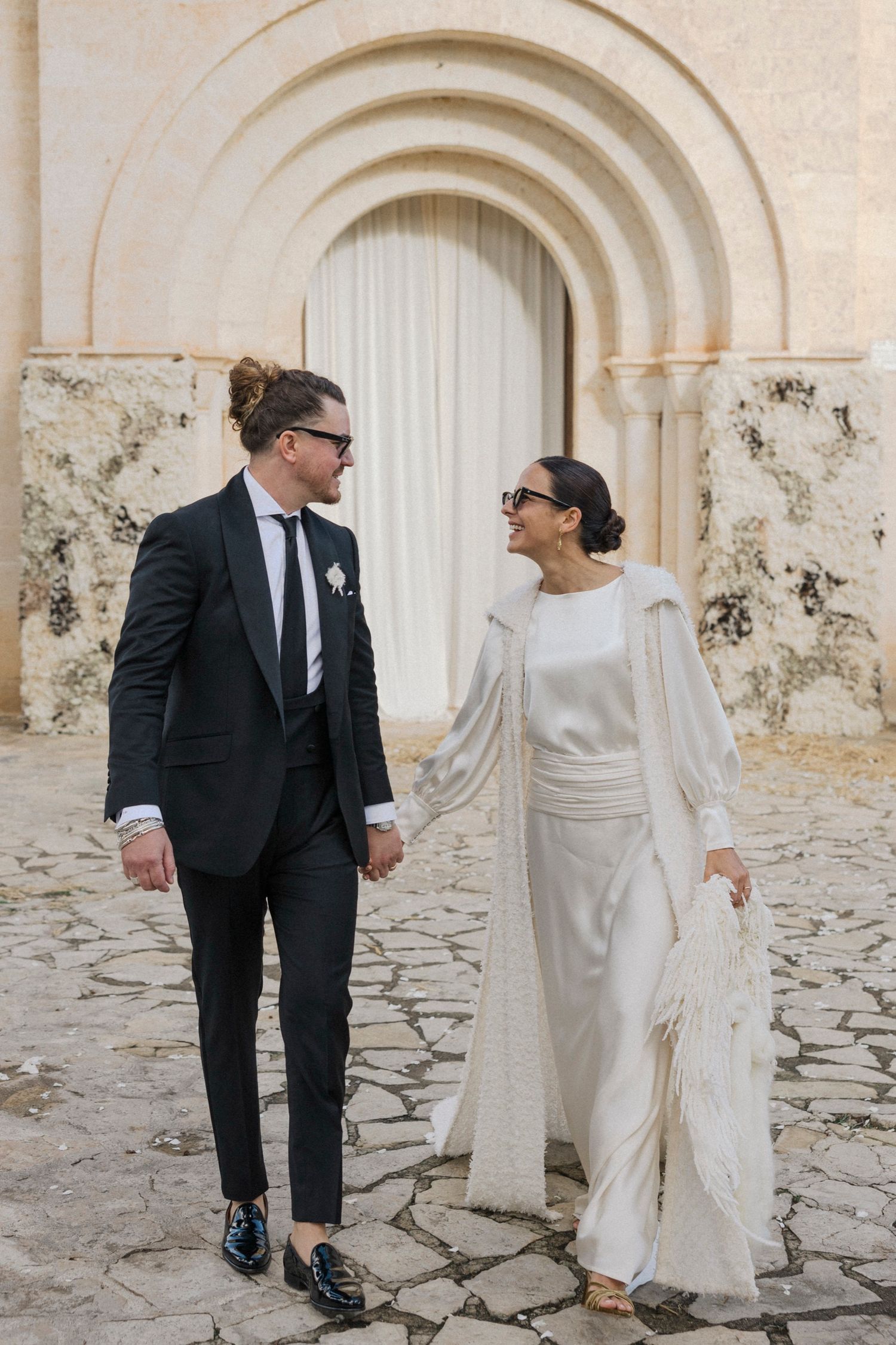 Candid moment of newlyweds sharing a laugh in front of historic church entrance.