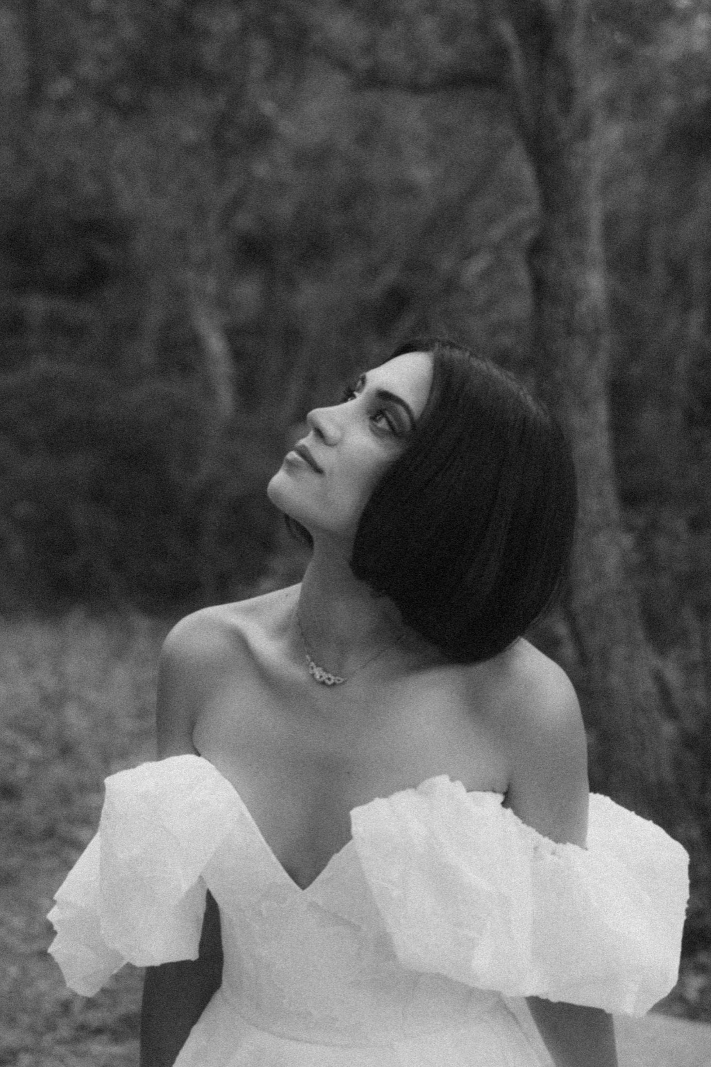 A person in a white off-shoulder dress poses dramatically in a black and white artistic portrait series.