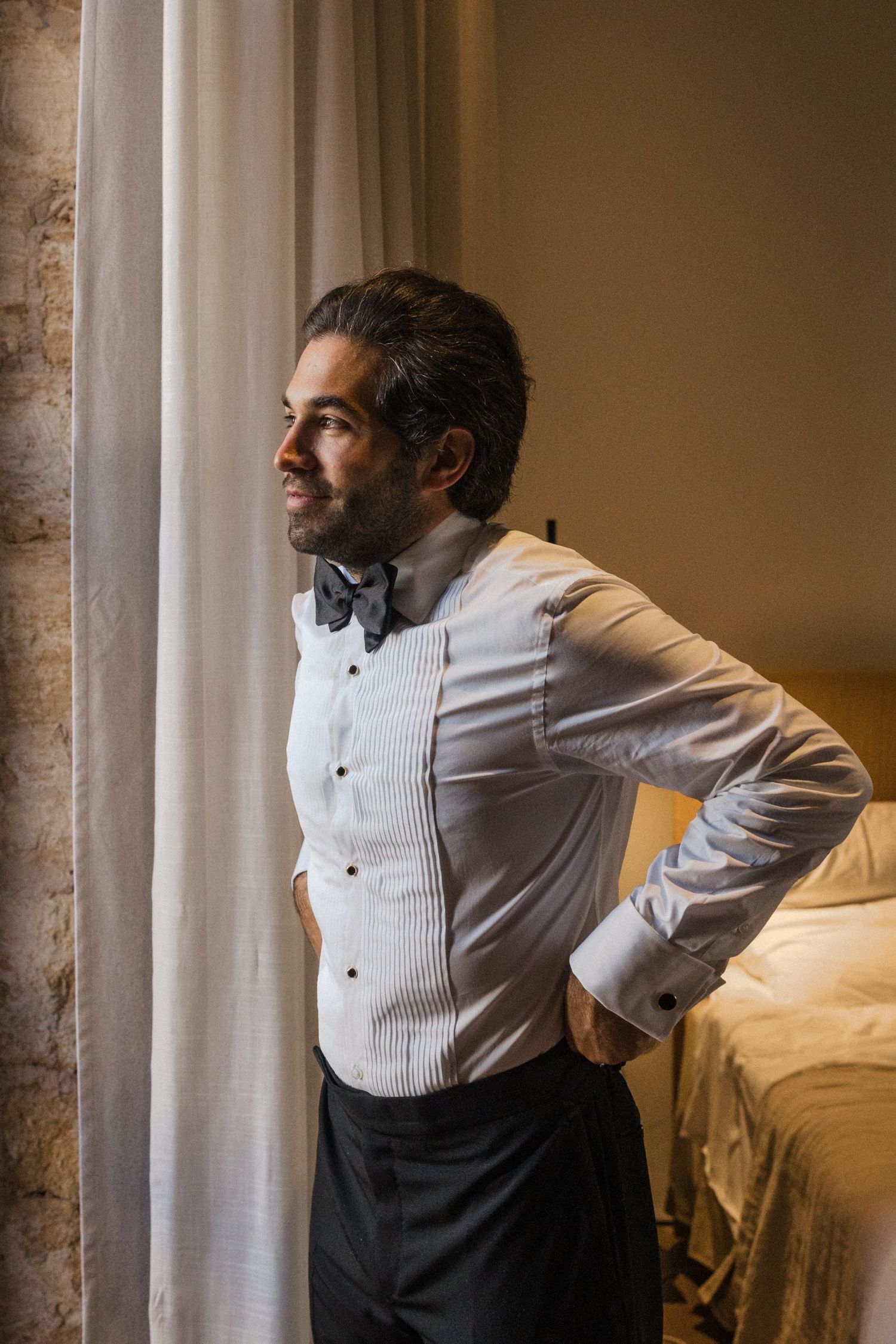 Person in formal attire adjusts their posture while getting ready in a warmly lit room.