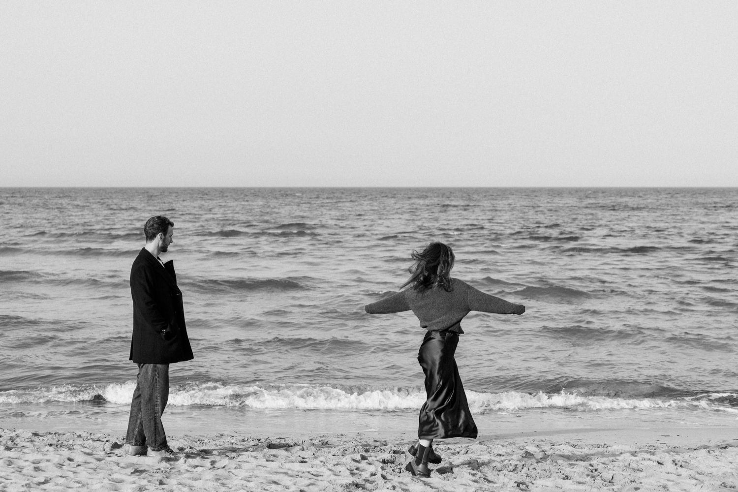 A series of black and white beach photographs showing people walking along the shoreline at sunset.