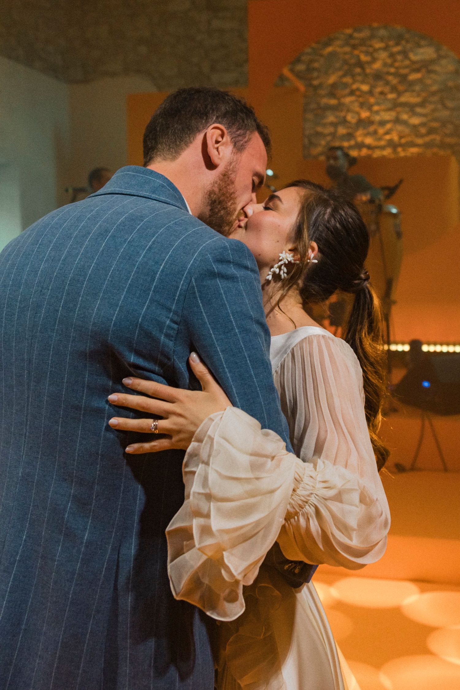 A romantic wedding moment captured as a couple shares their first dance in a warmly lit venue with stone walls.