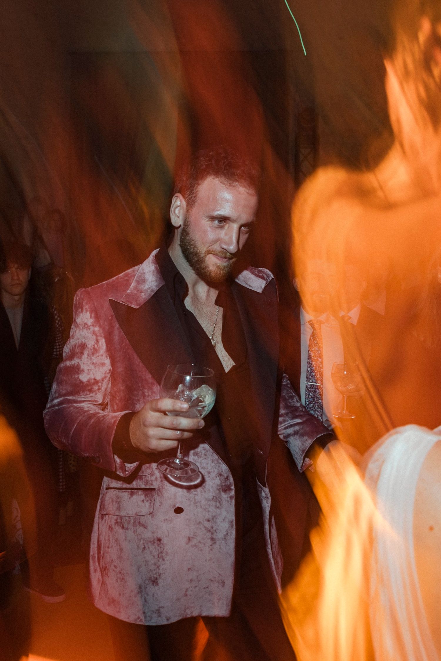 Person in a dark setting illuminated by dramatic orange lighting effects holding a drink.