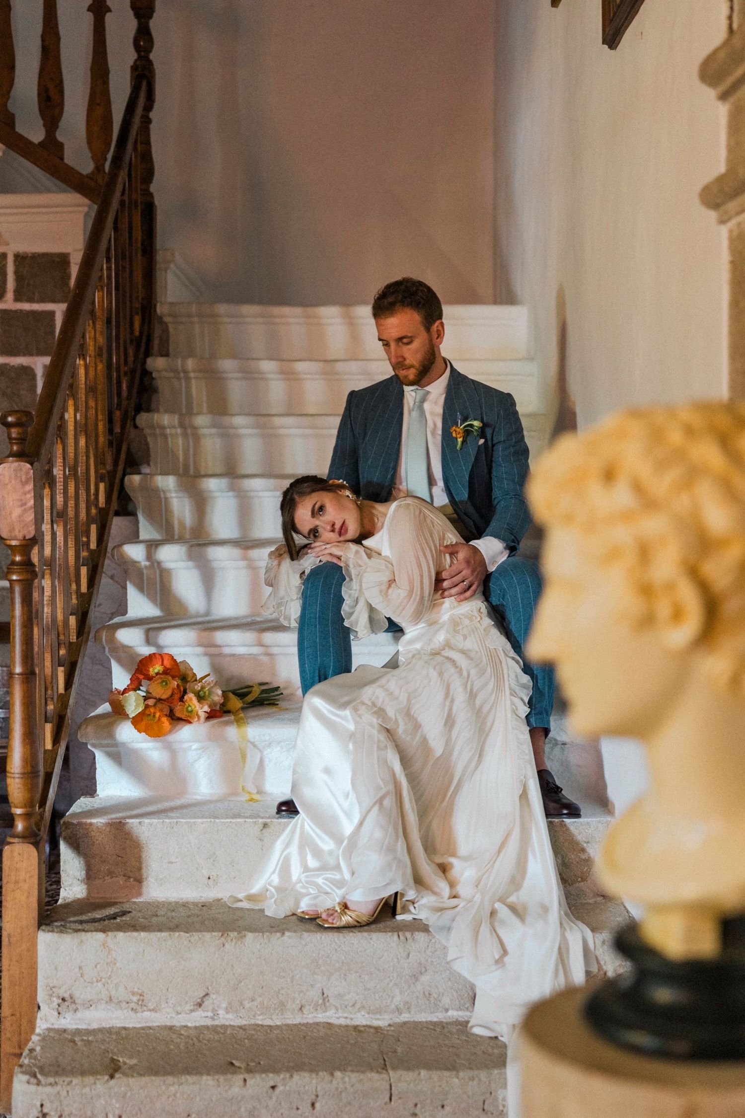A couple shares a tender moment on a white staircase during their wedding photoshoot.