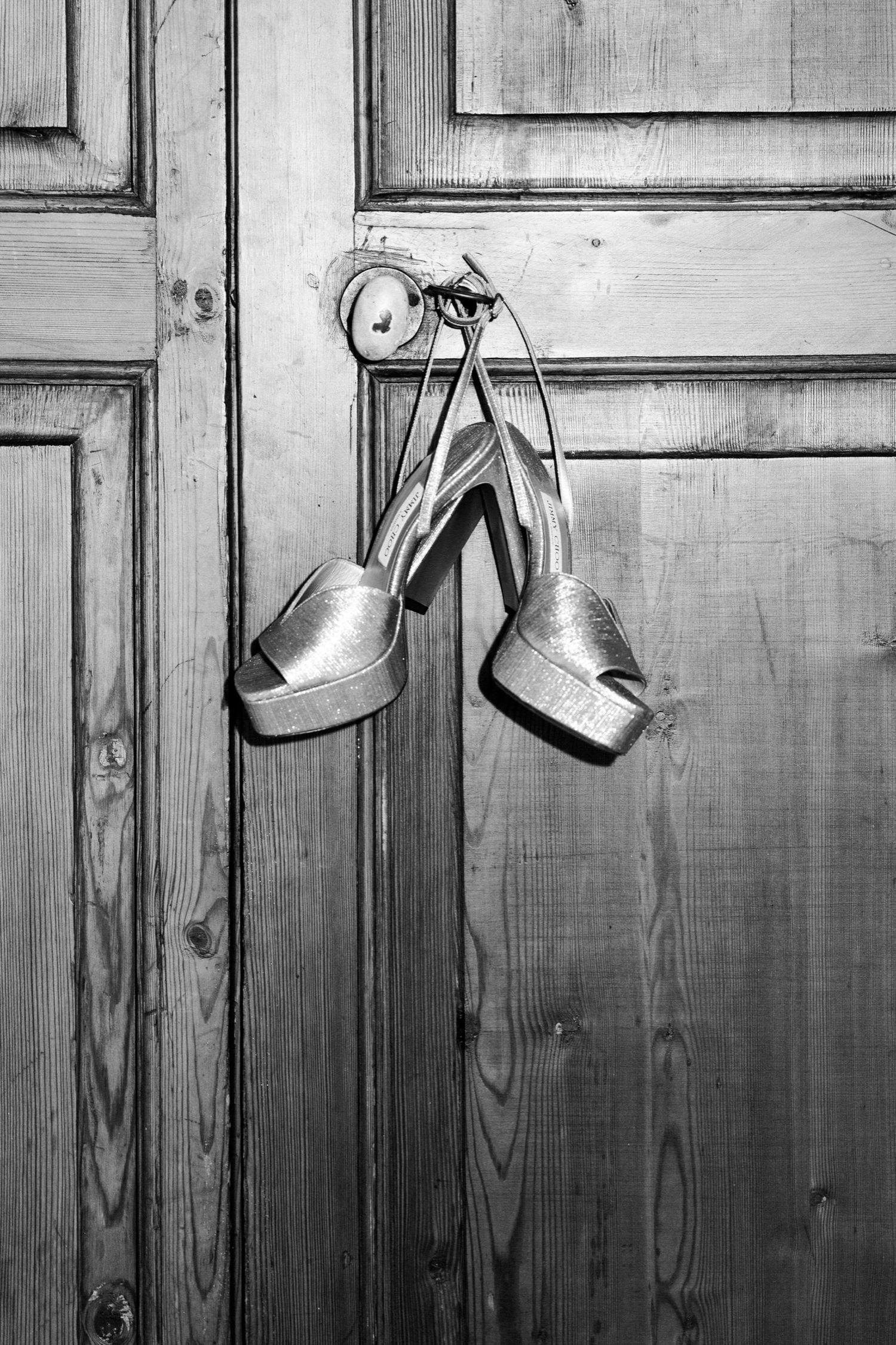 Silver bridal shoes arranged in a row against a rustic wooden wall creating an elegant wedding detail shot.