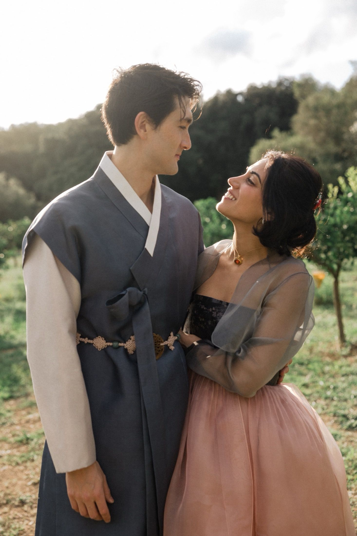 A couple shares intimate moments in a garden setting wearing formal attire in mauve and gray tones.