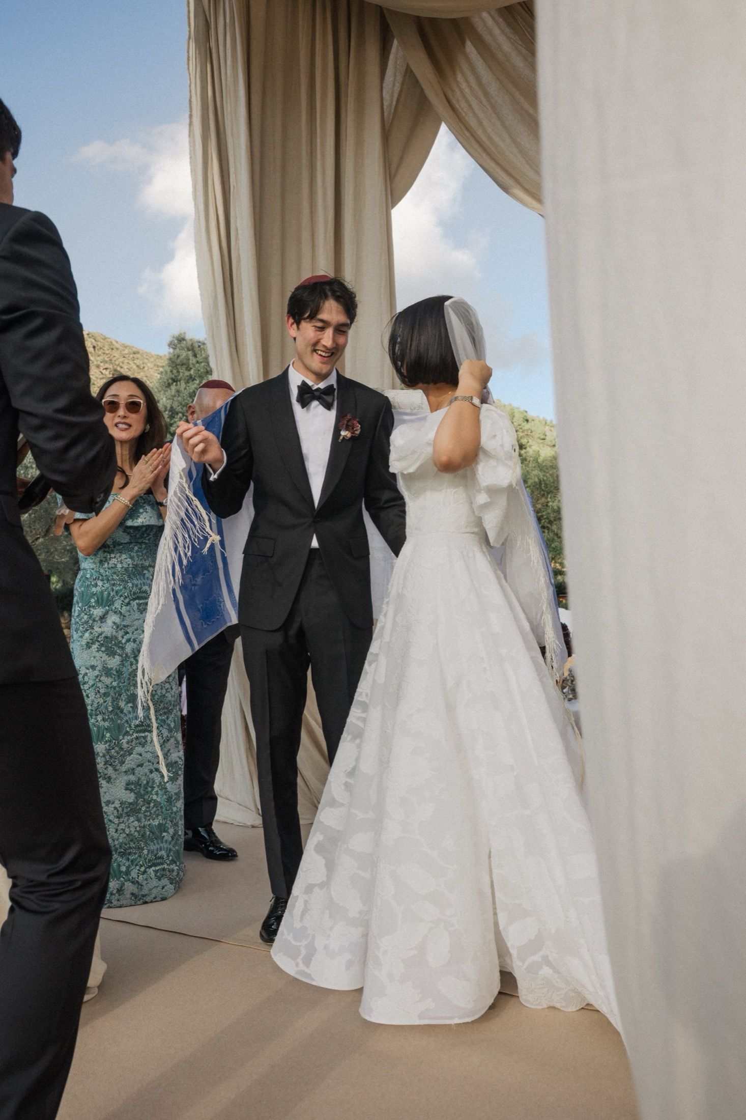 A wedding party stands together near white curtains during an outdoor ceremony.