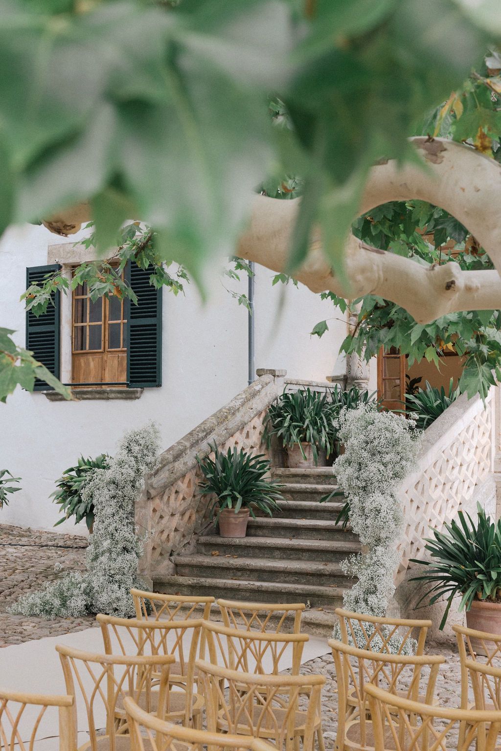 Mediterranean-style venue with stone steps and wooden shutters surrounded by greenery.
