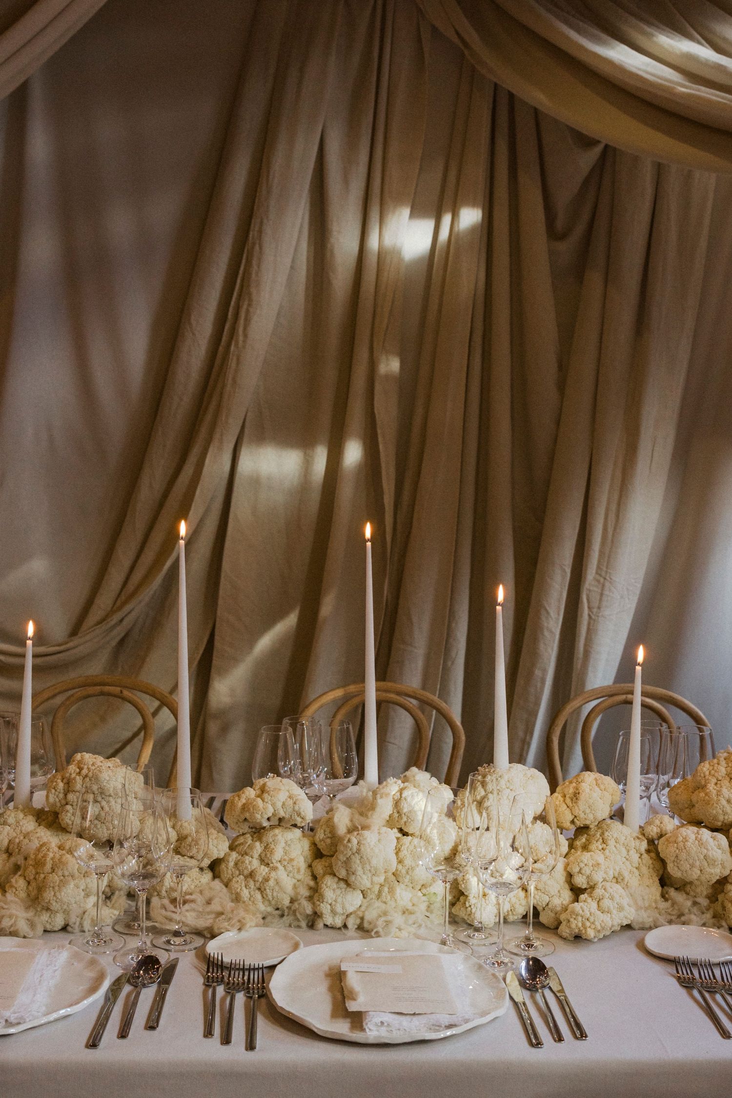 Close-up of white floral arrangements and taper candles on a formal dining table with draped fabric backdrop.