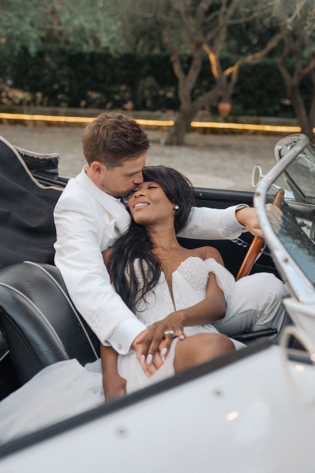 Couple embracing in a vintage white convertible car during sunset.