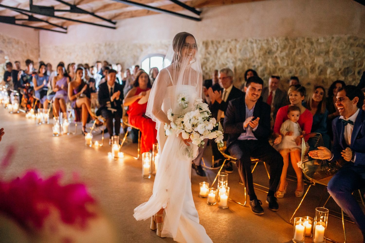 Candlelit wedding reception with guests seated along rustic stone walls and warm lighting.