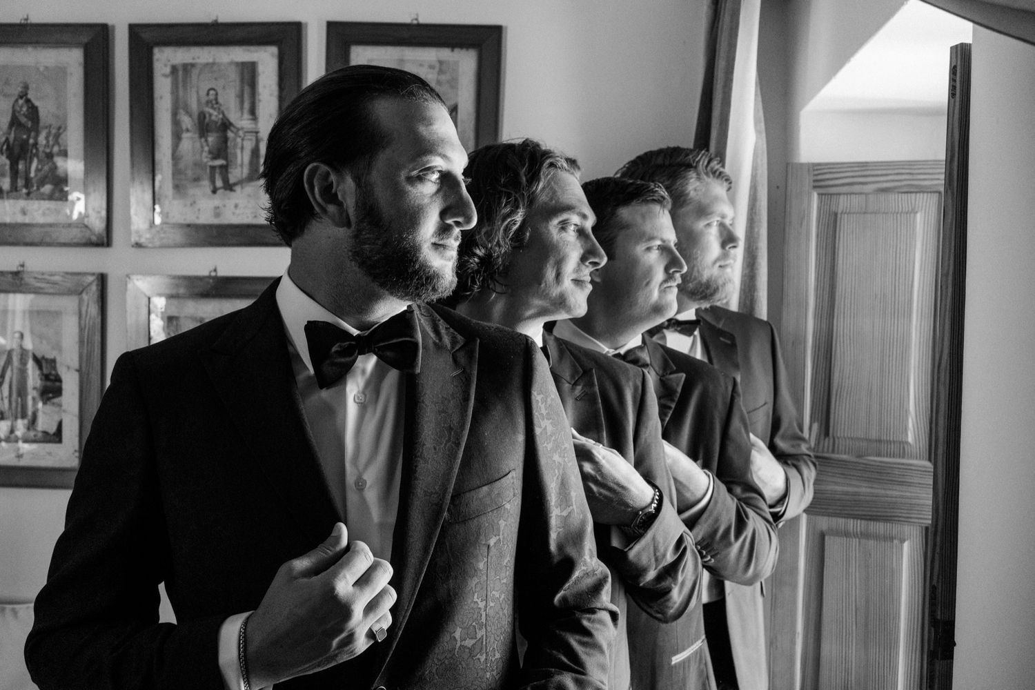 Group of formally dressed guests looking out a window in black and white photography.
