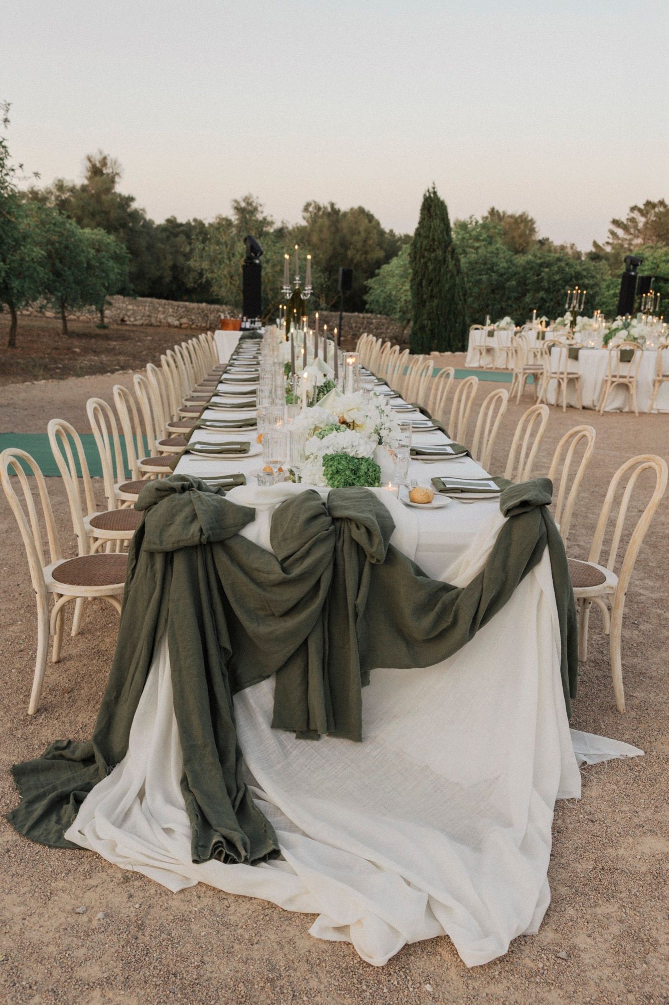Long wedding reception table with olive green chair draping and white tablecloths.