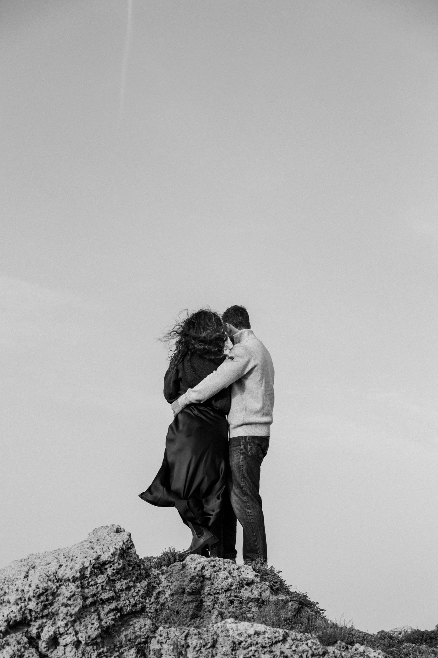 A series of black and white photographs showing a couple embracing on a hilltop against a light sky.