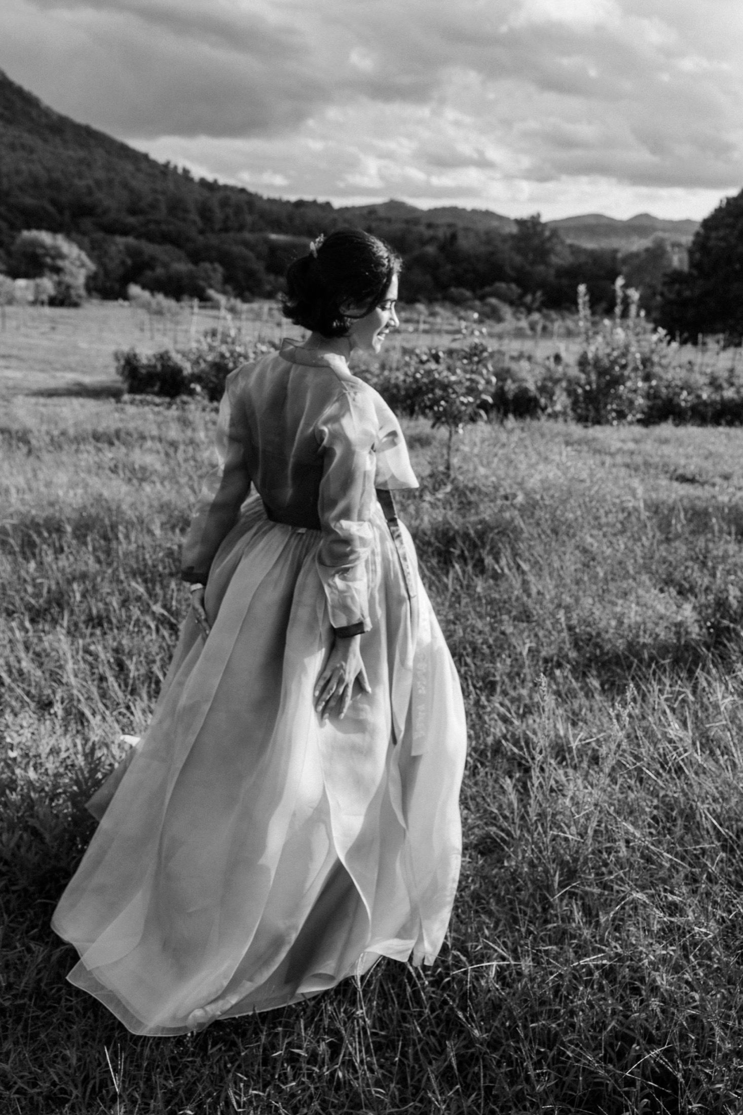 A black and white series of photos showing a flowing white dress in a grassy meadow with mountains in the background.