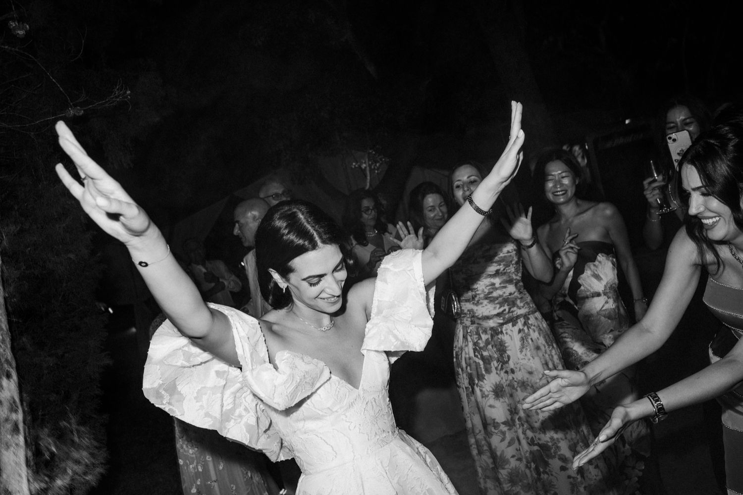 People dancing and celebrating with raised arms at a lively party in black and white.