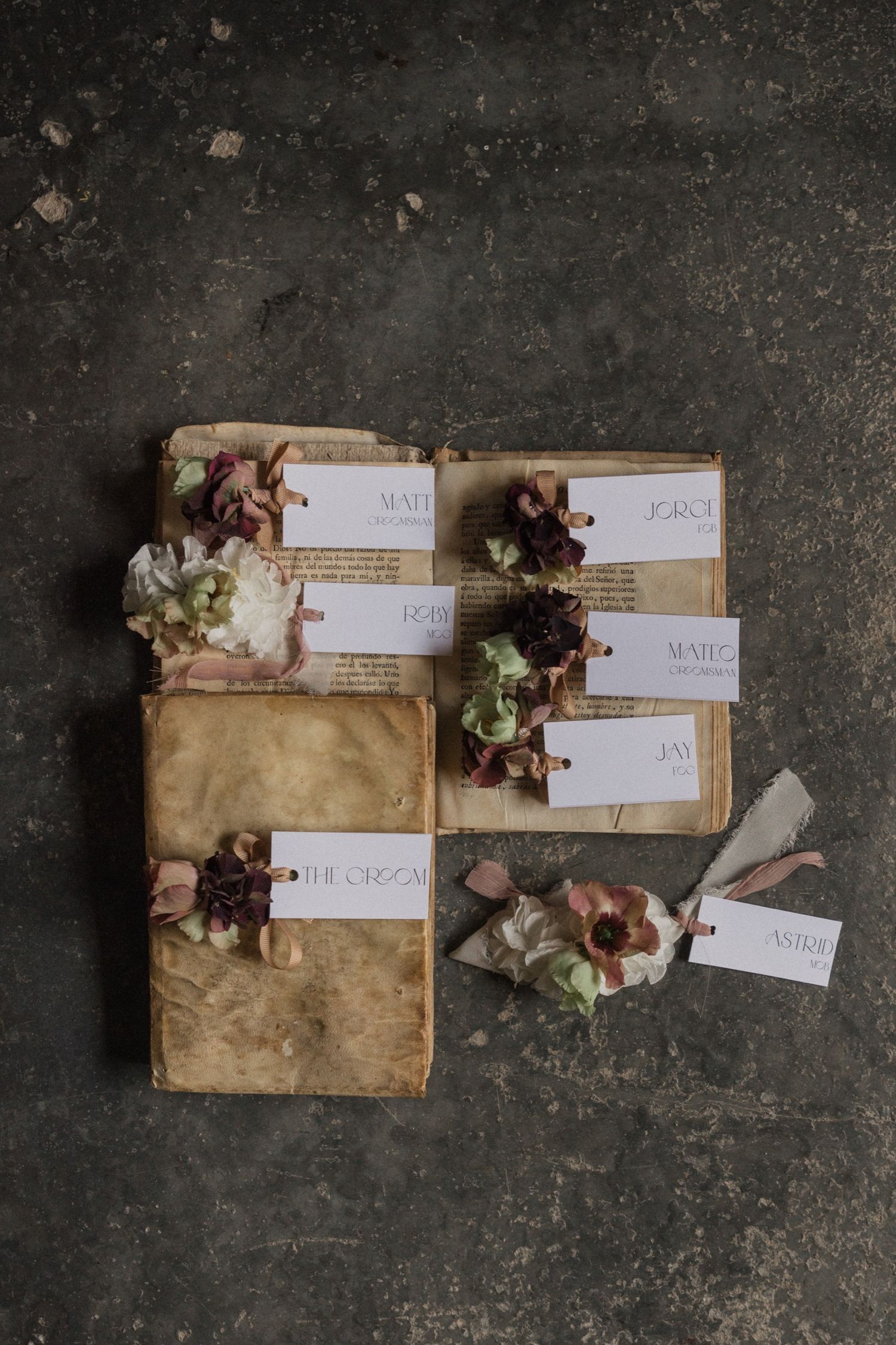 Vintage paper envelopes decorated with dried flowers and name tags arranged on dark textured surface.