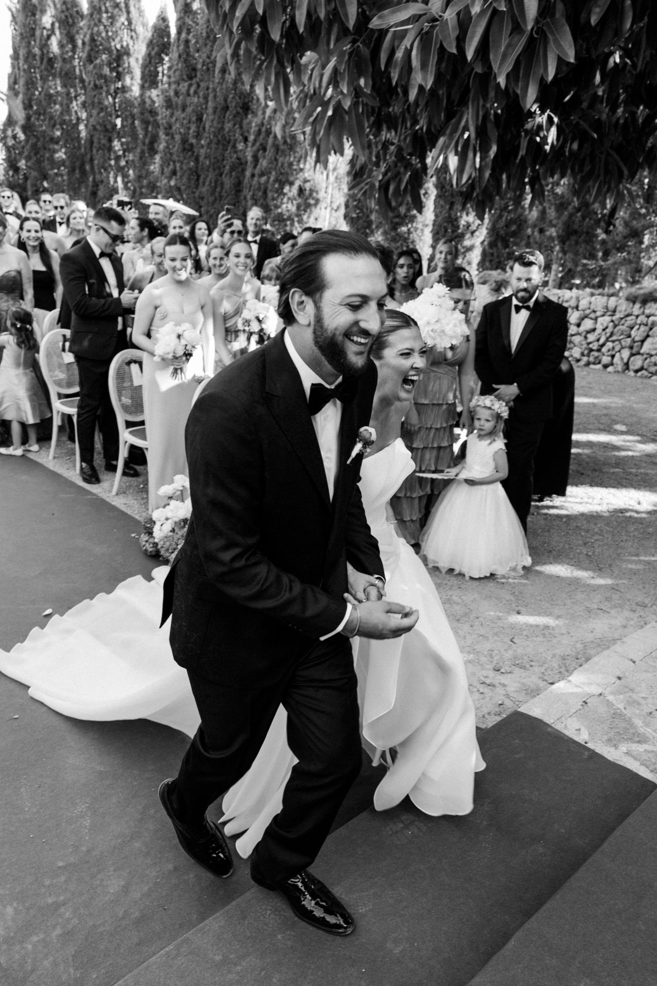 Wedding celebration on green carpet with cypress trees in background.
