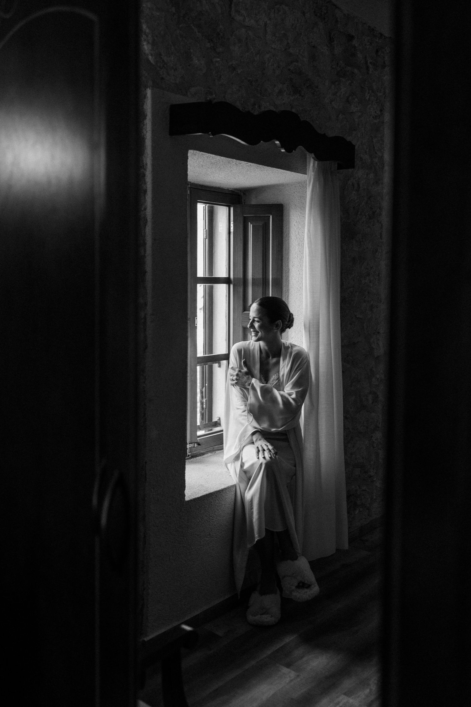A moody black and white photo shows a figure in white near a bright window.