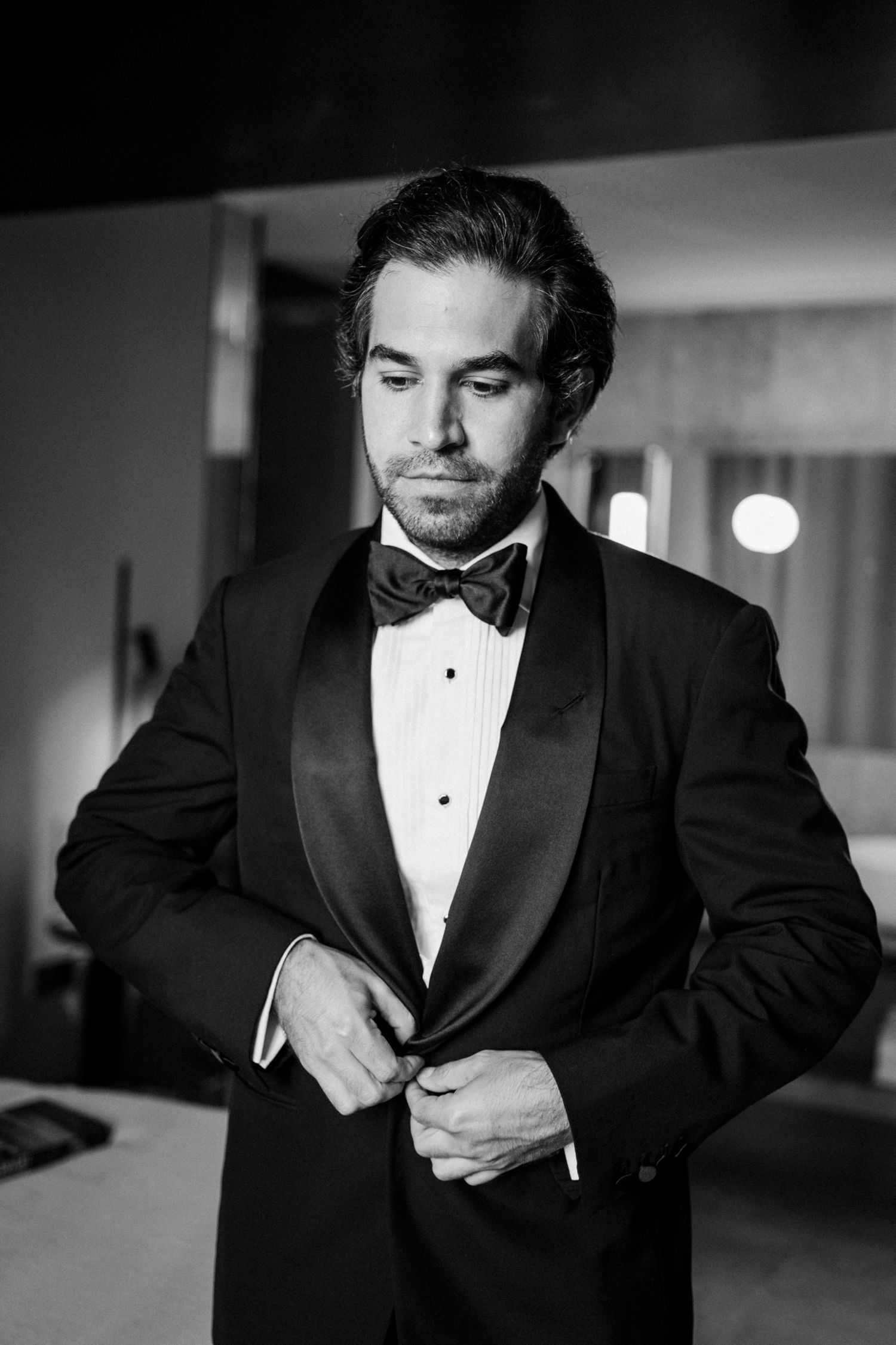 Black and white photo series showing someone adjusting a tuxedo and bow tie while getting dressed for formal event.