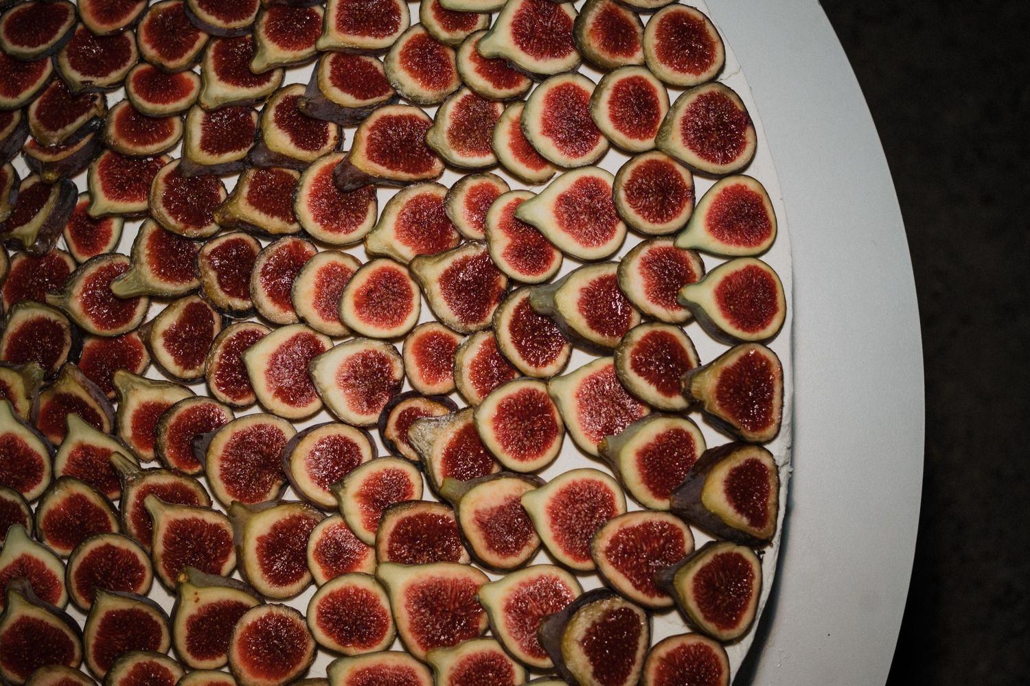 Close-up view of perfectly arranged red fig tarts displayed on a white serving platter.