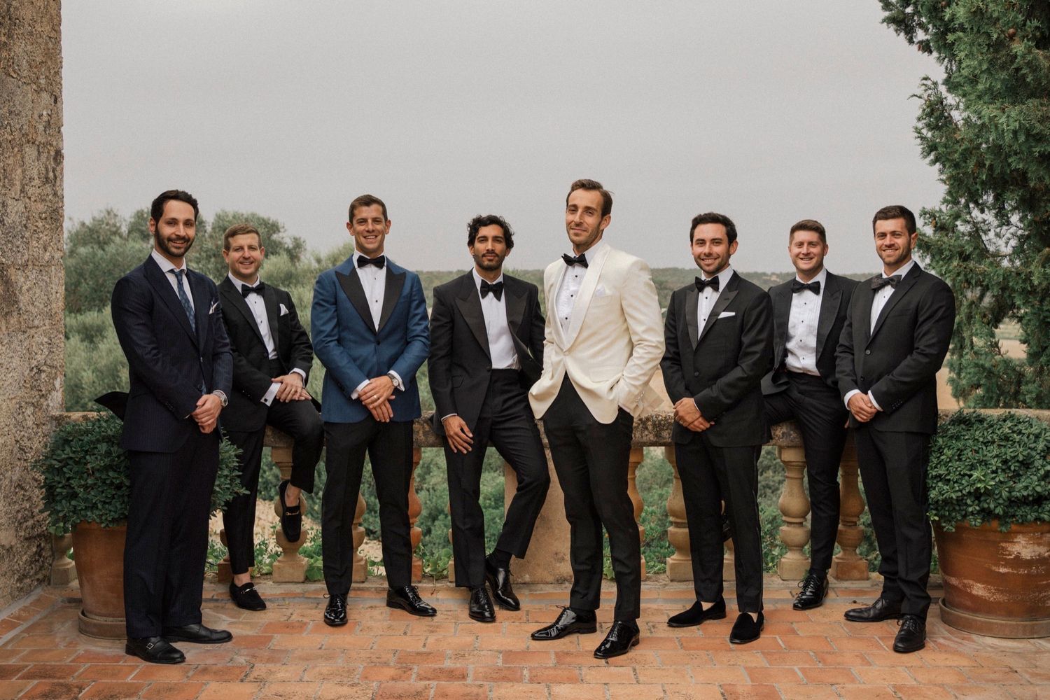 Wedding party in formal attire posing outdoors with groomsmen wearing black suits.