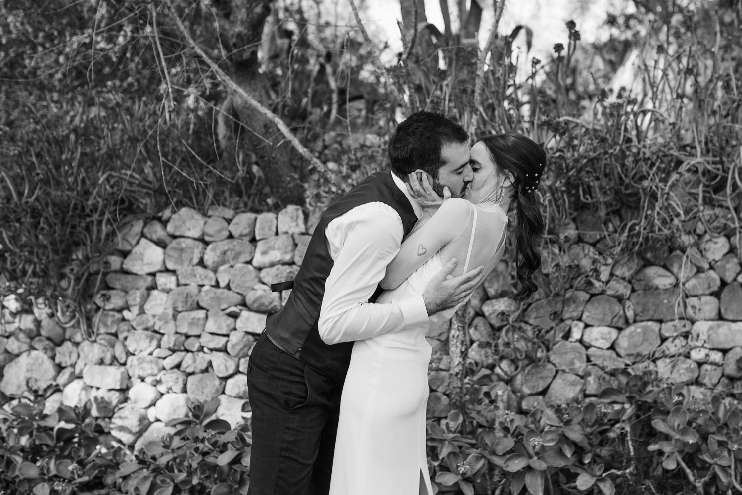 Black and white romantic wedding photo series showing intimate moments against a stone wall backdrop.