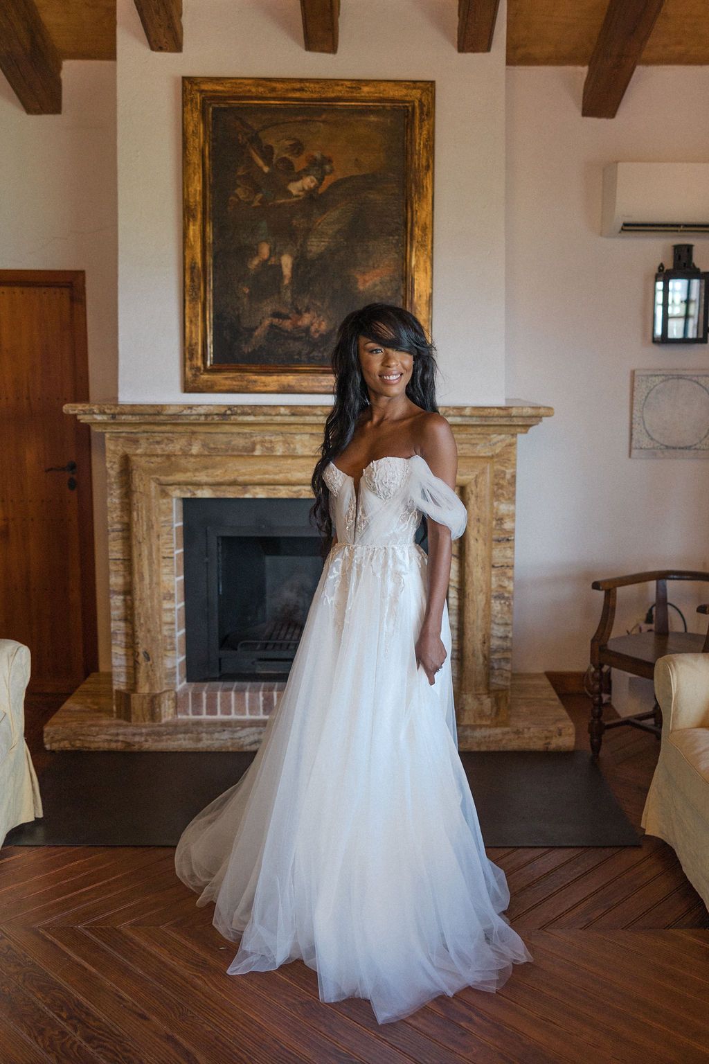 Bridal portraits in flowing white gown against rustic room with wooden beams.