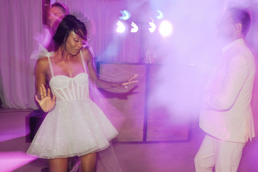 A couple performs a romantic dance sequence in a purple-lit venue during a wedding reception.