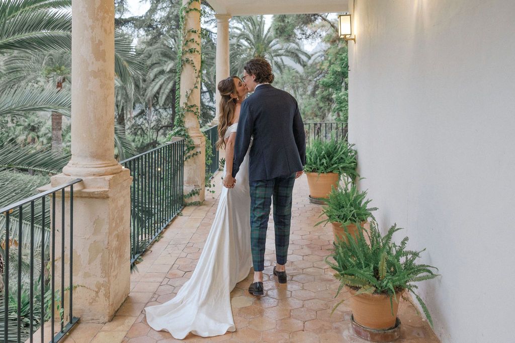 Wedding couple walks along Mediterranean terrace with palm trees and lanterns.