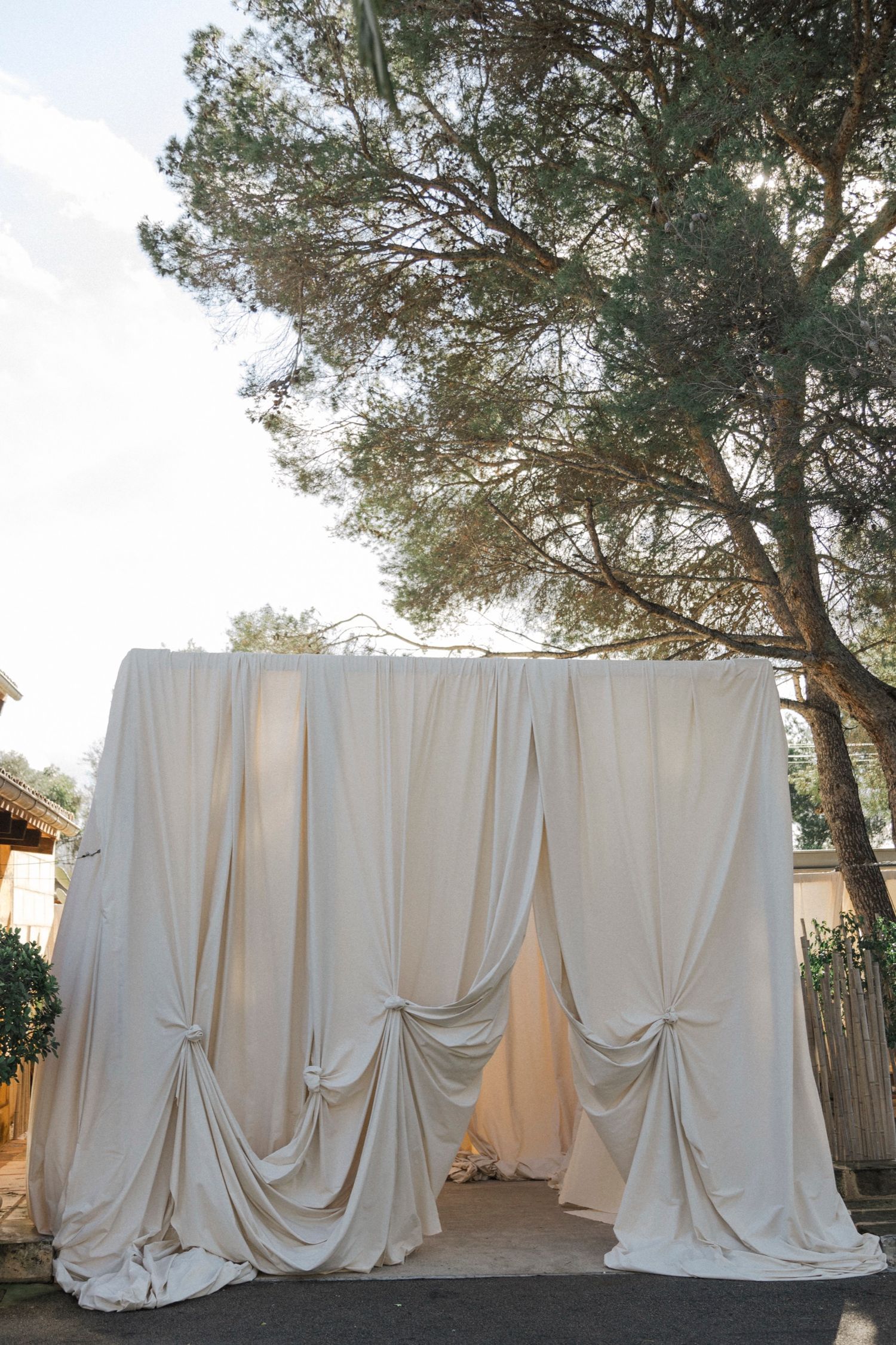 Long white drapes create an elegant outdoor wedding backdrop against pine trees.