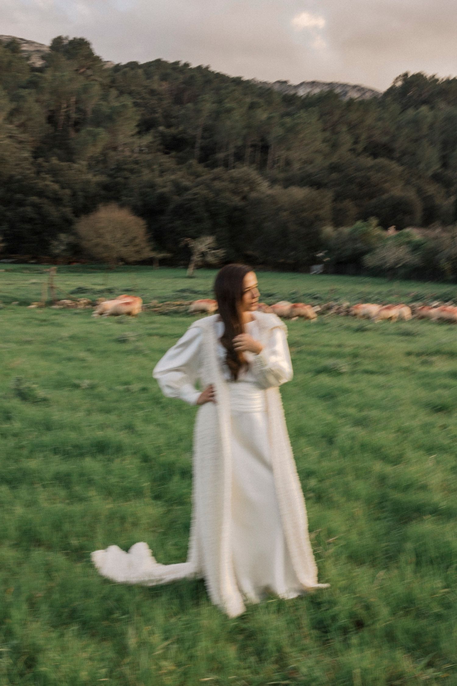 Person in white dress spins gracefully in green field with mountains visible.
