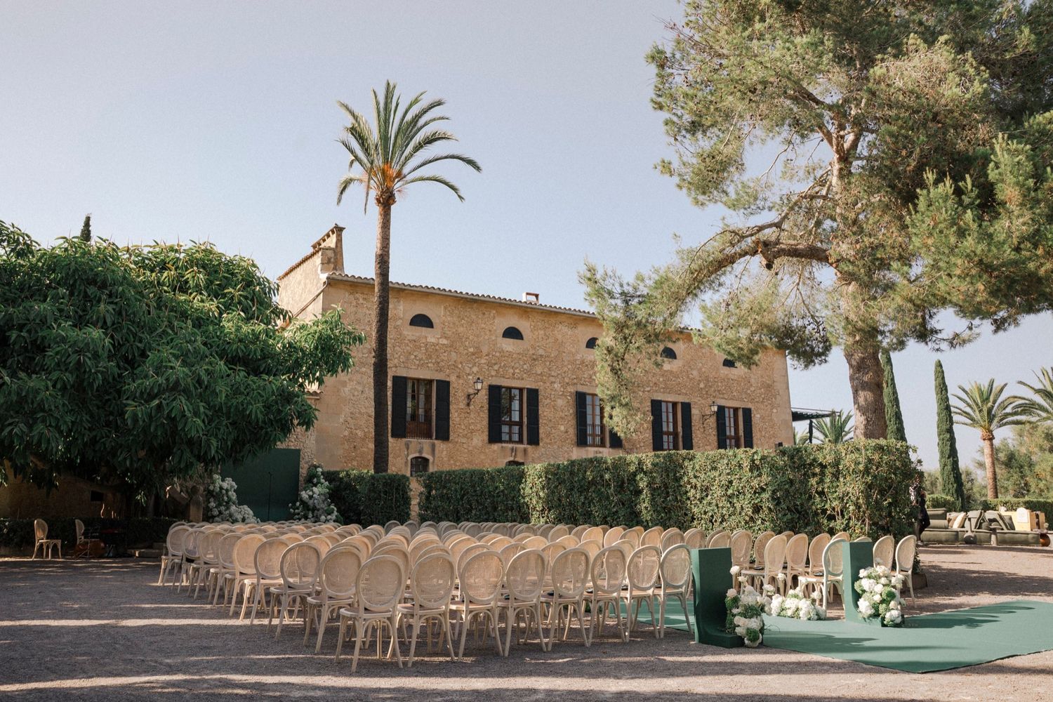 Panoramic view of an outdoor wedding venue with chairs arranged in rows against a stone building.
