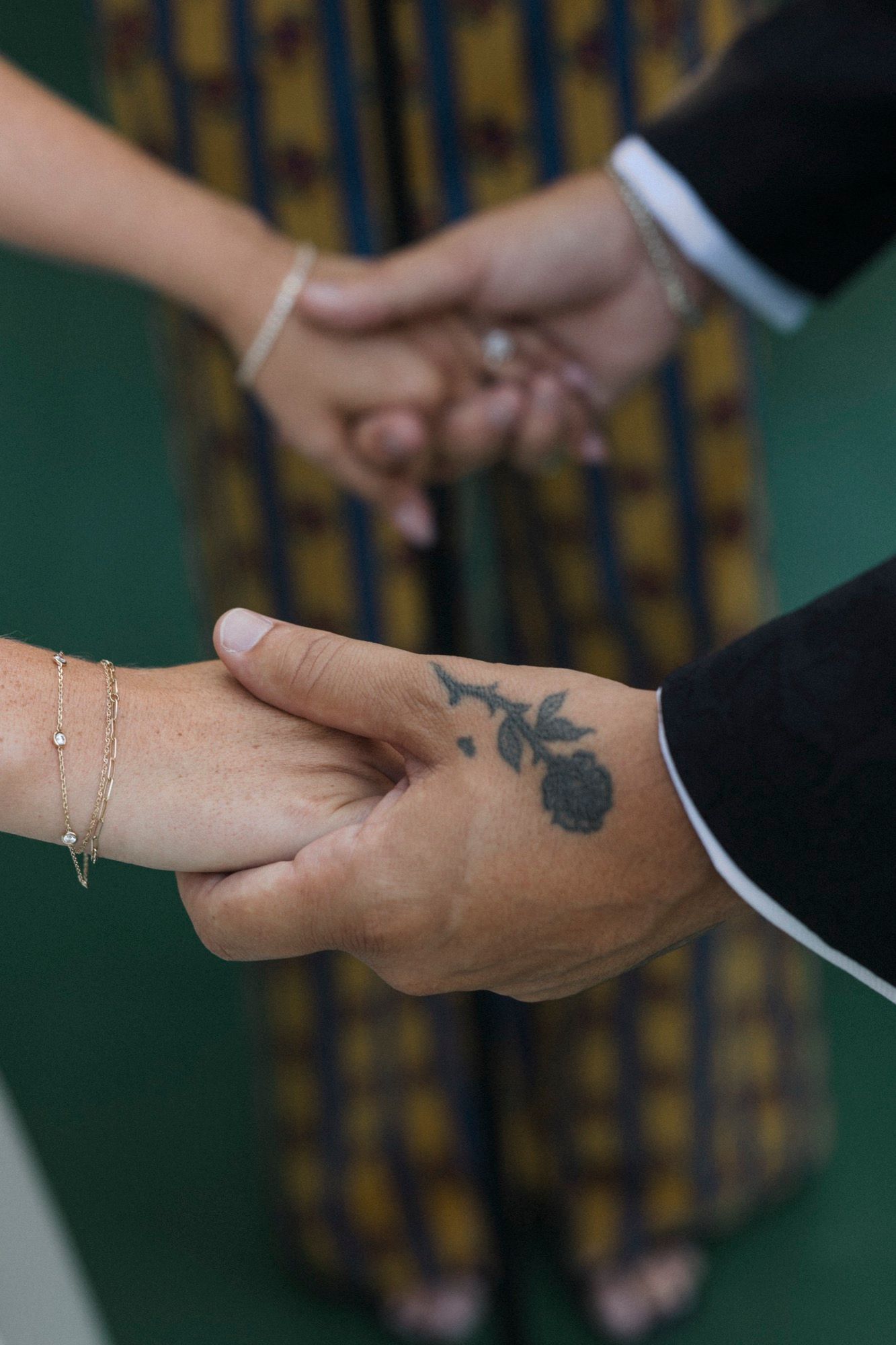 Close-up of clasped hands showing a floral tattoo during a wedding ceremony.