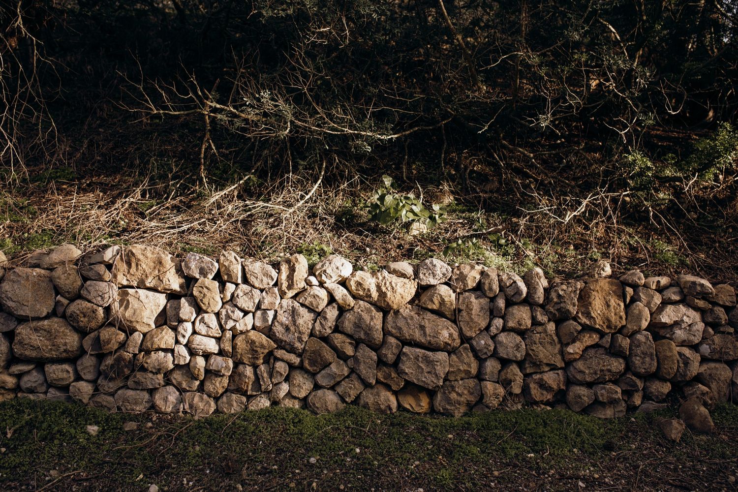 A row of natural stone retaining walls built along a hillside with varying textures and patterns.
