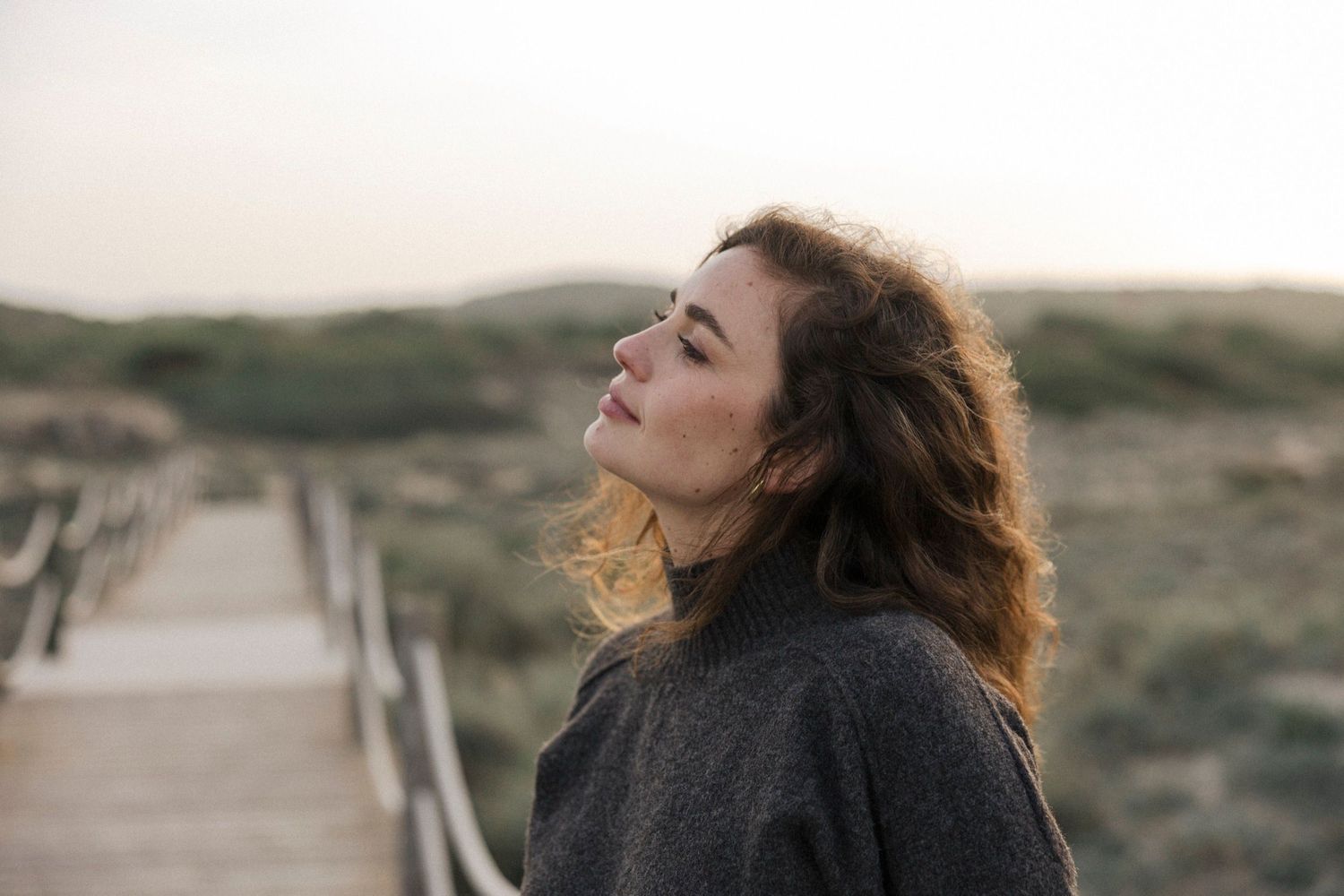 Woman with windswept hair laughs joyfully against scenic mountain backdrop at sunset.