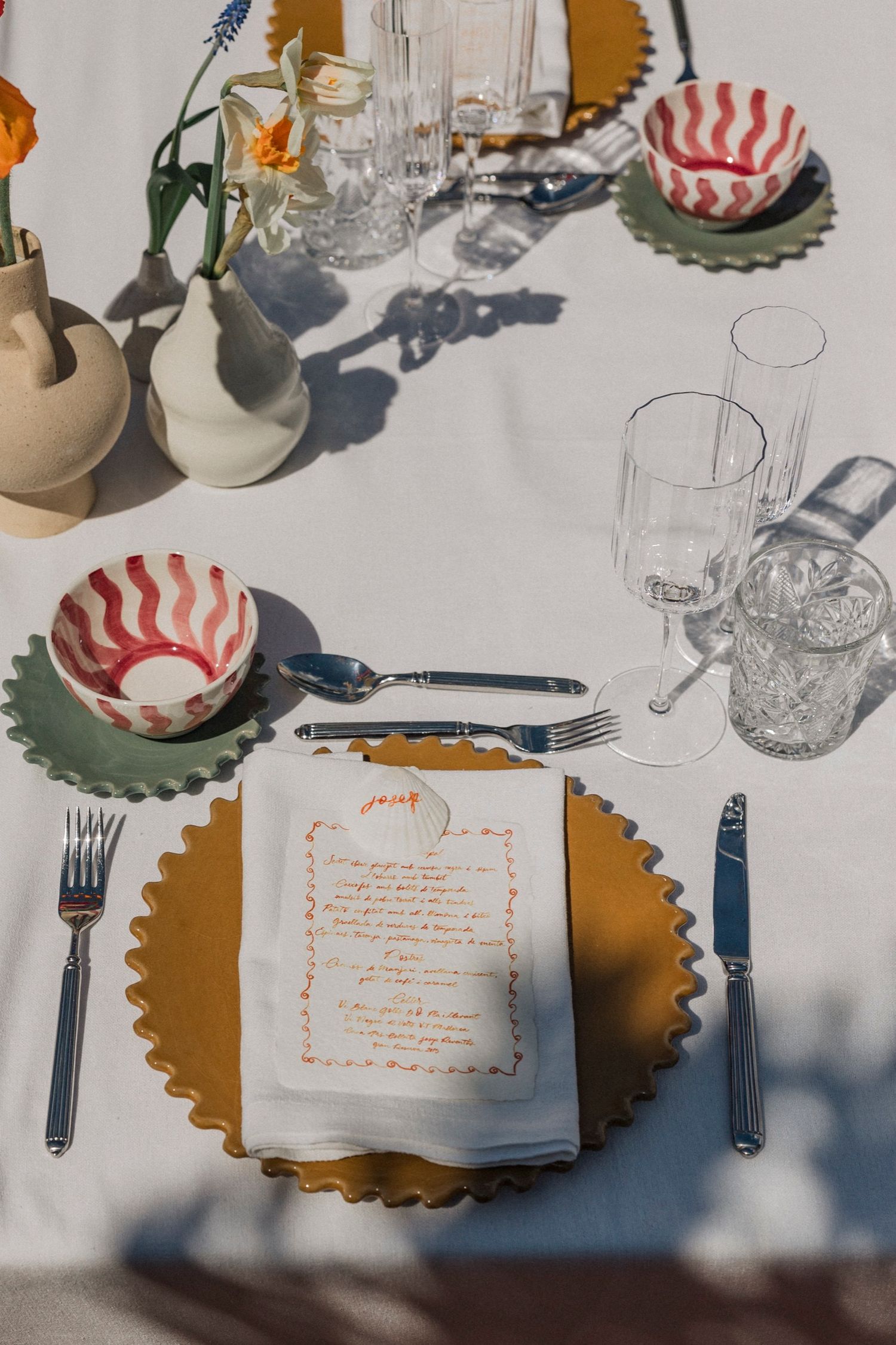 Place settings at a formal event with scalloped gold charger plates, menus, and red and white striped bowls on white tablecloths.
