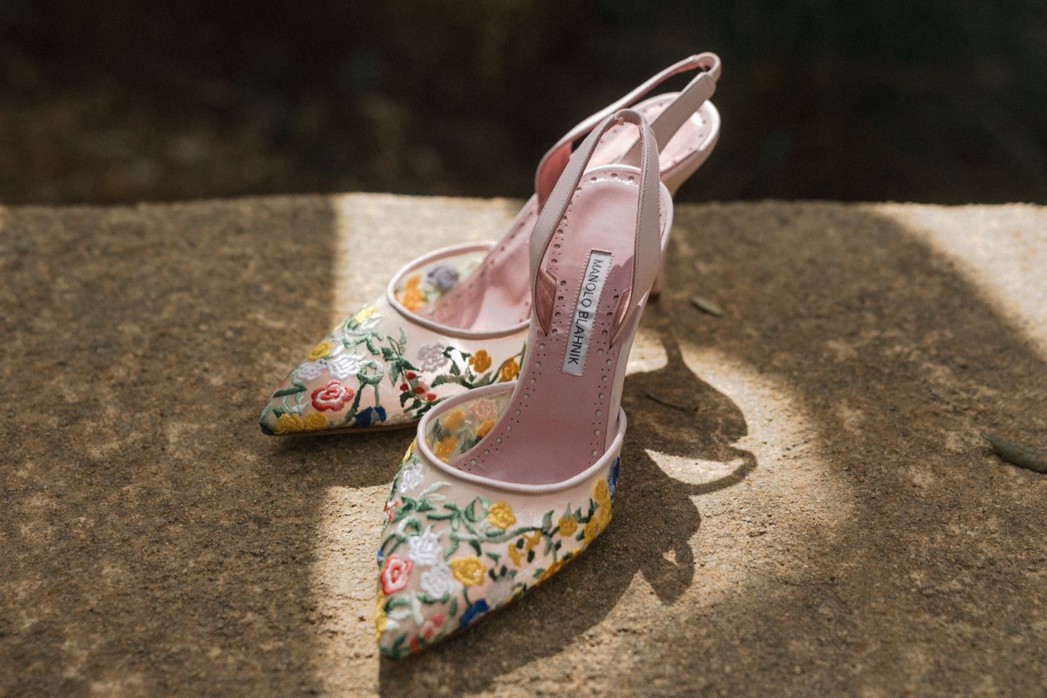 Floral embroidered slingback heels in pink with delicate flower patterns cast a shadow in sunlight.
