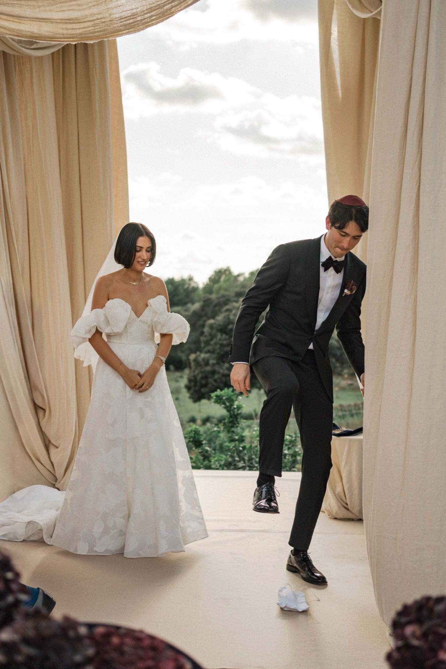 Playful newlyweds share a fun moment under elegant draped fabric at their outdoor wedding.