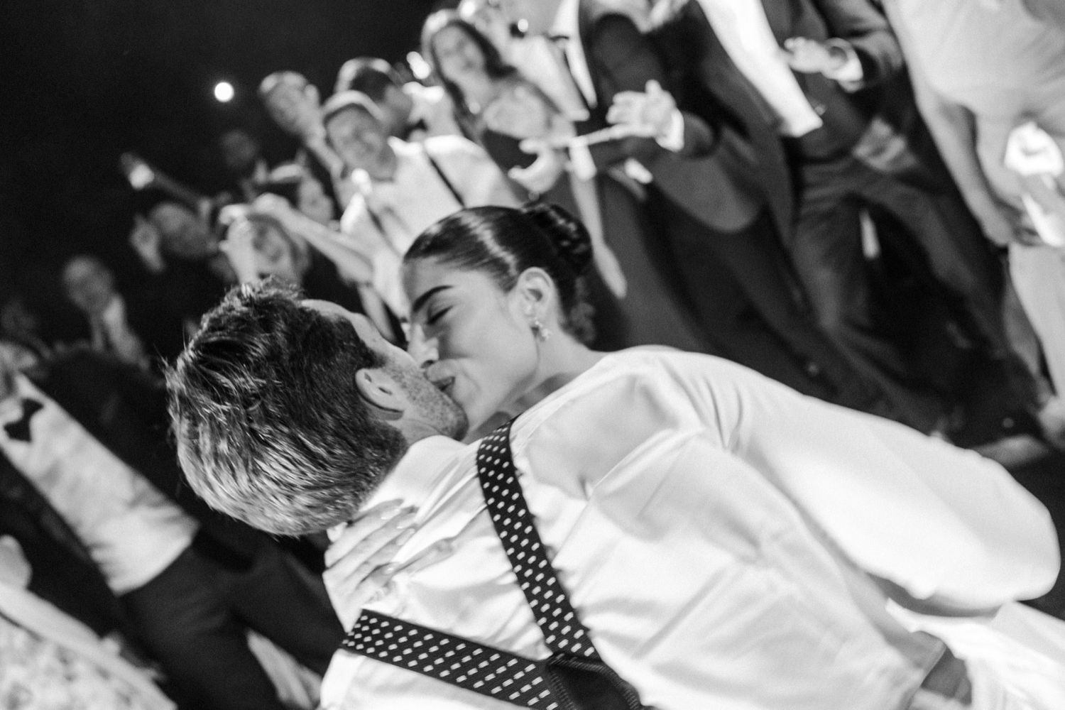 A black and white photo of two people dancing energetically at a party wearing polka dot suspenders.