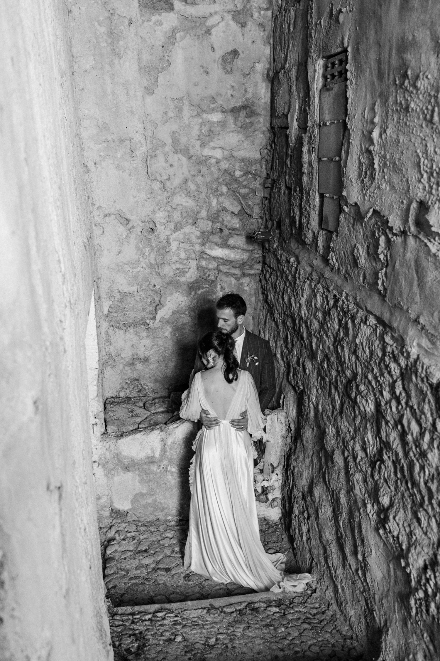 A romantic black and white photo of a couple embracing in a rustic stone passageway.