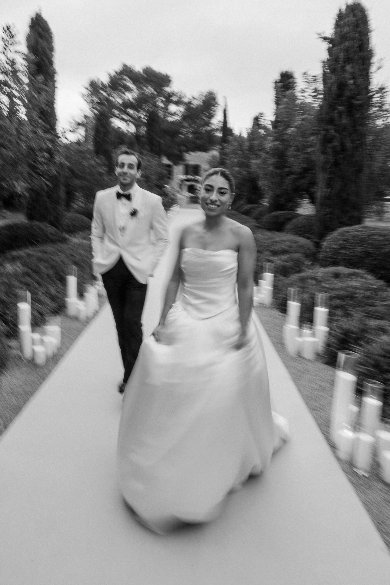 A sequence of black and white wedding photos showing a couple spinning and dancing together on a tree-lined path.