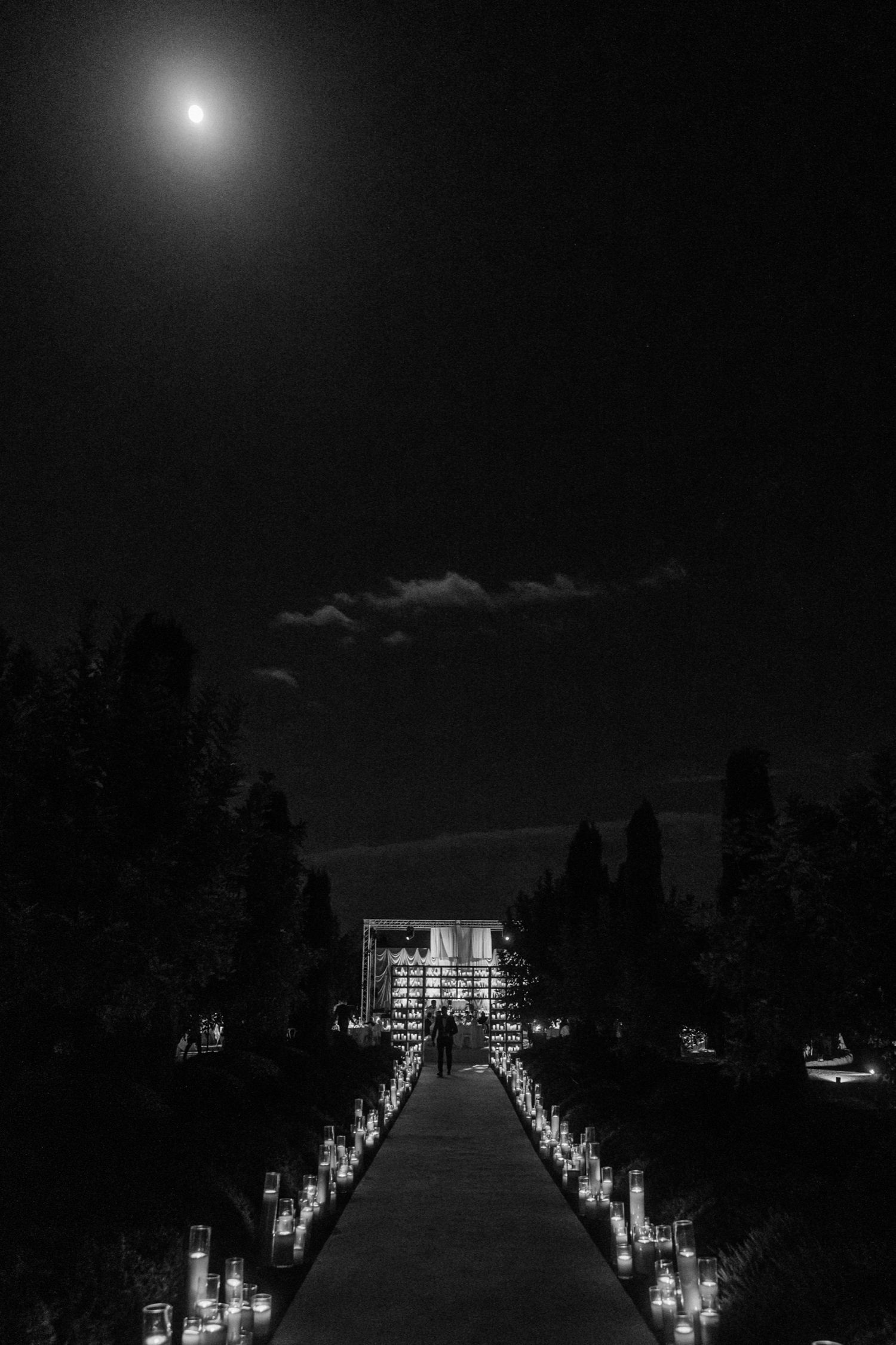 Illuminated pathway at night with glowing candles and lights creating a mystical atmosphere under the moonlit sky.