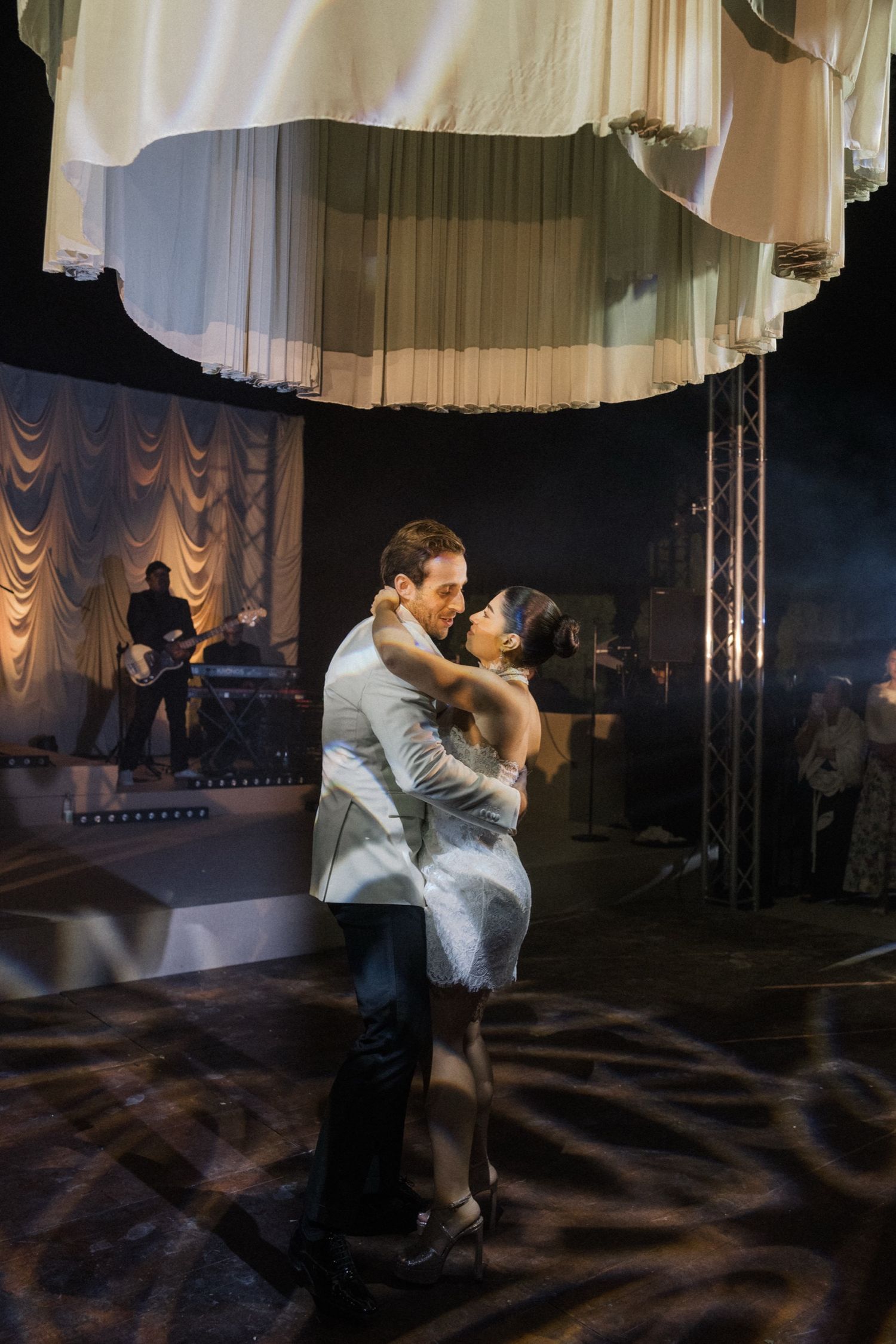 A couple shares a romantic dance in an elegant ballroom with dramatic lighting and curtained backdrop.